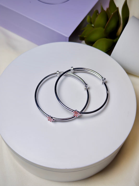 Two silver baby kada with pink monkey charms on a white surface.