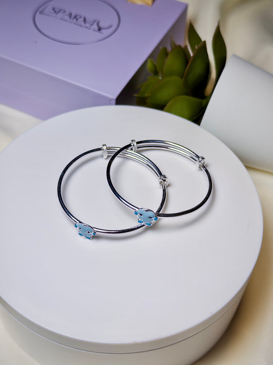 Silver baby kada with blue cartoon on a white surface, with a purple box in the background.