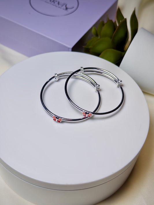 Two silver baby kada with red butterfly on a white surface with a purple box in the background.