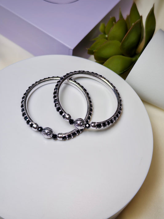Two silver bracelets with black beads on a white surface.