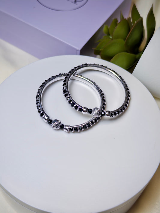 Two silver baby kada with black beads on a white surface.