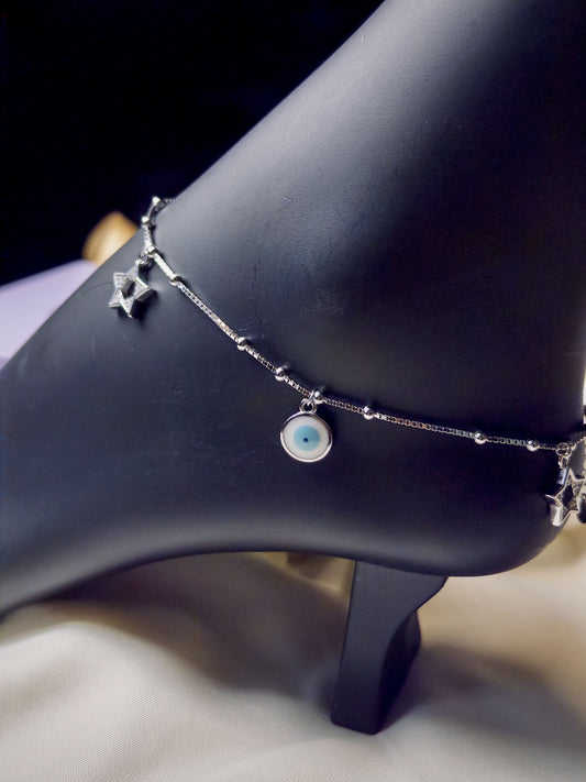 Silver anklet with star and eye charm on a black mannequin foot.