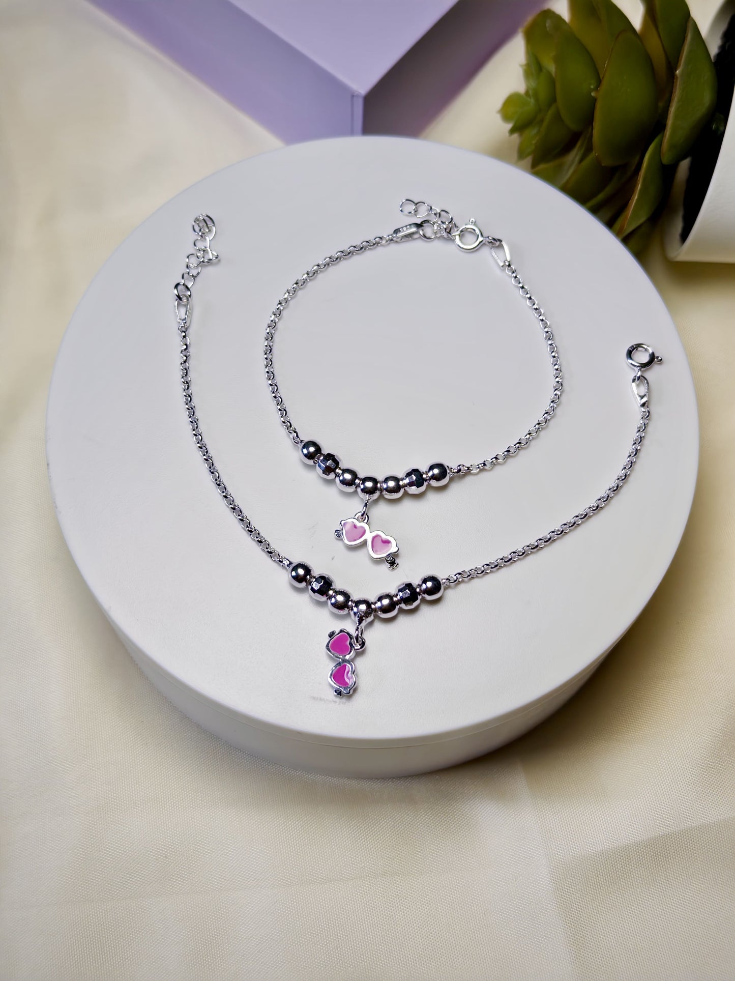 Silver anklets for kids with pink heart charm on a white surface