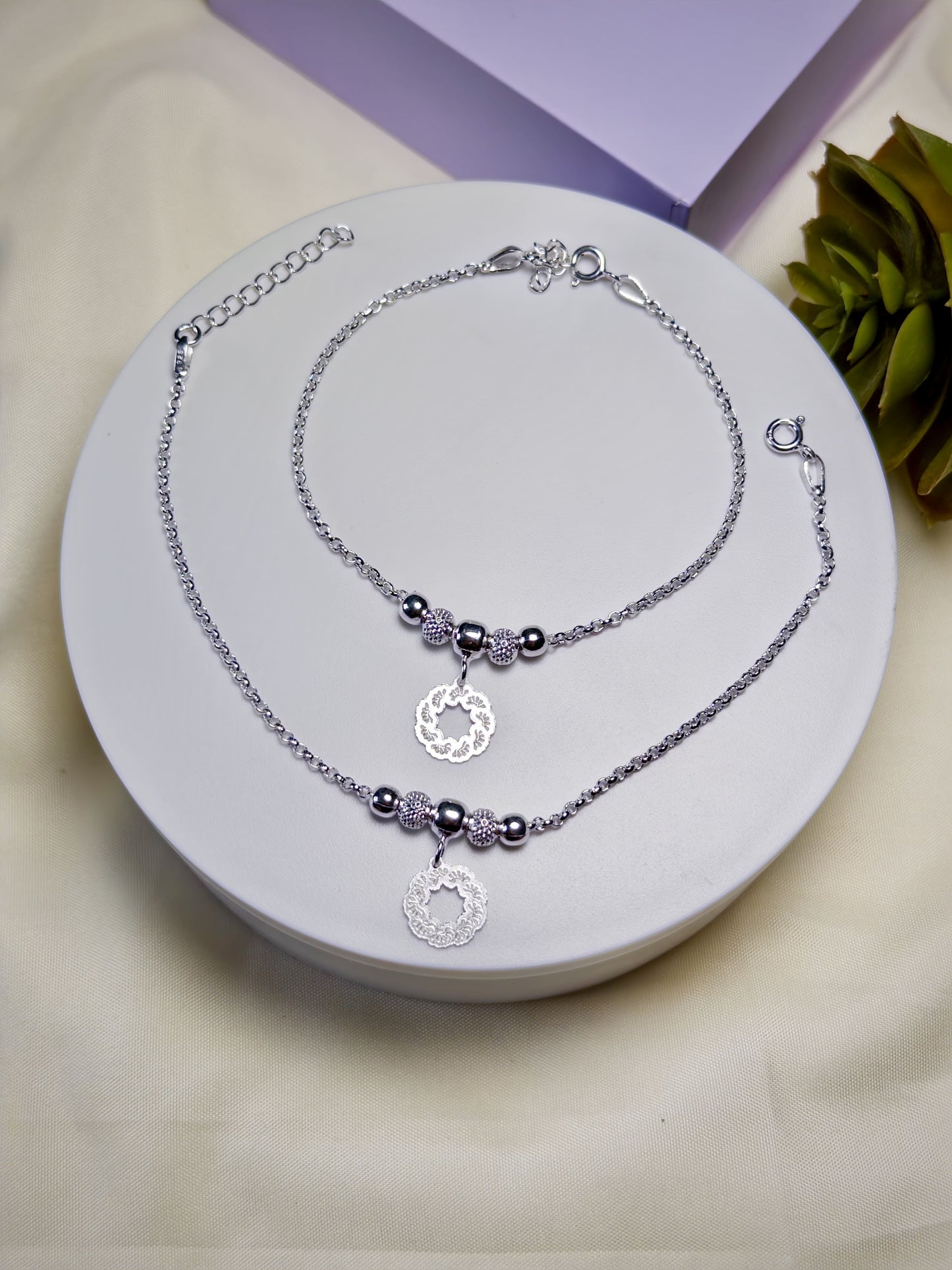 Pair of kids silver anklets with beads on a white surface