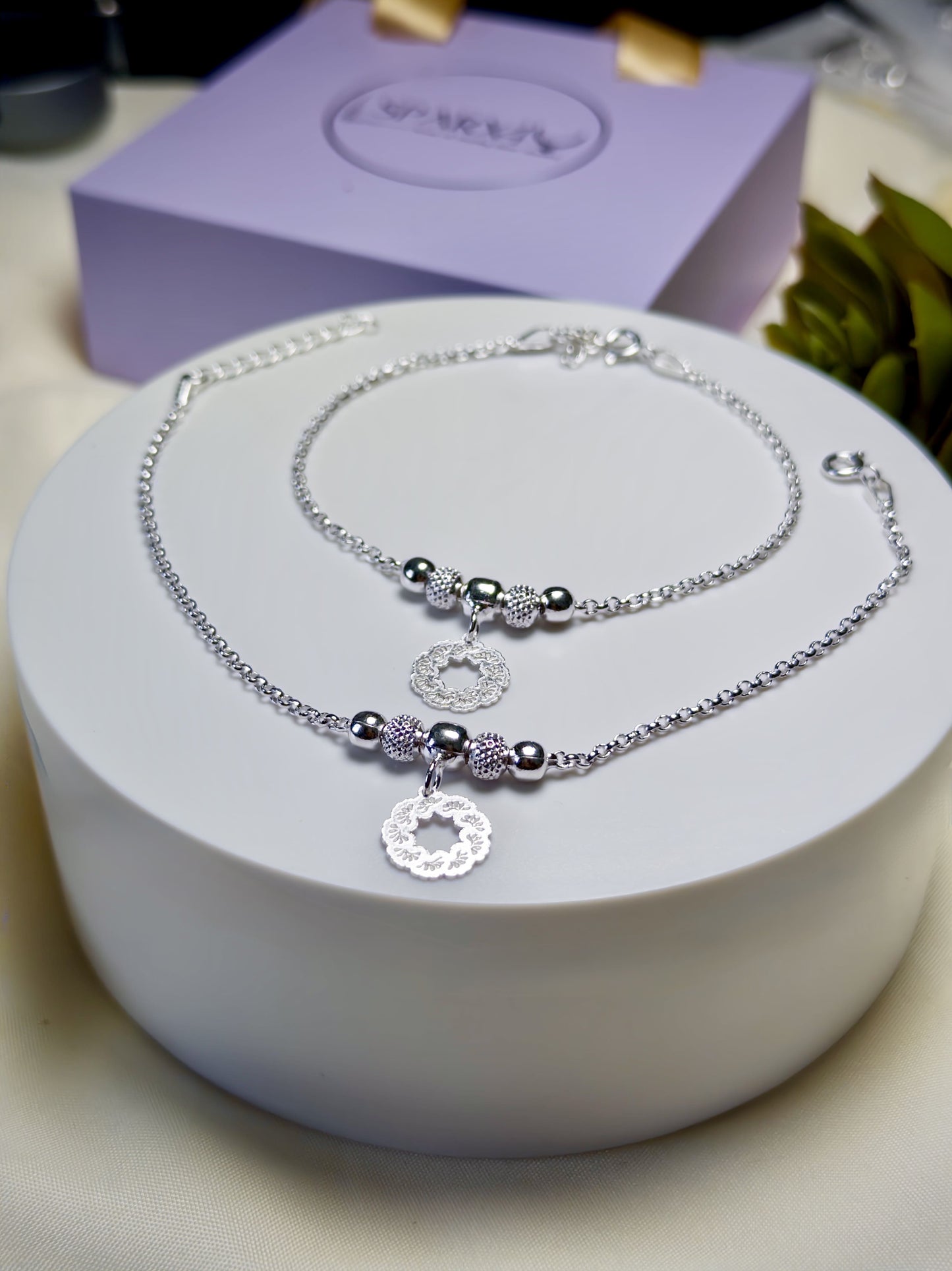 Kids silver anklets with beads on a white stand with a purple box in the background