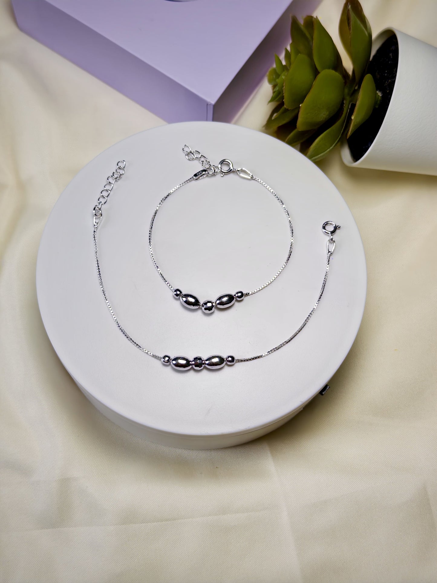 Kids silver anklets set on a white circular stand with a light background