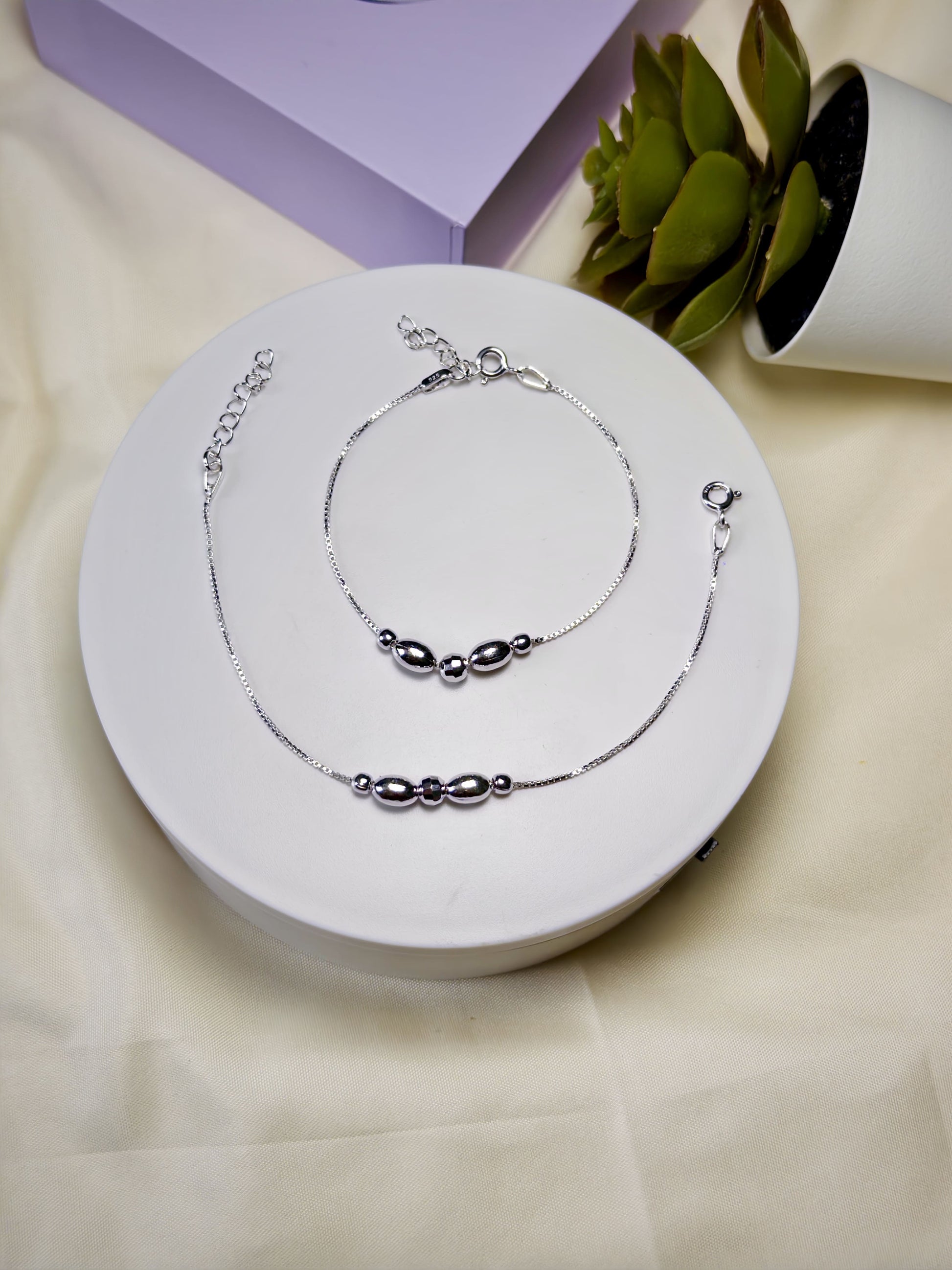 Kids silver anklets set on a white circular stand with a light background