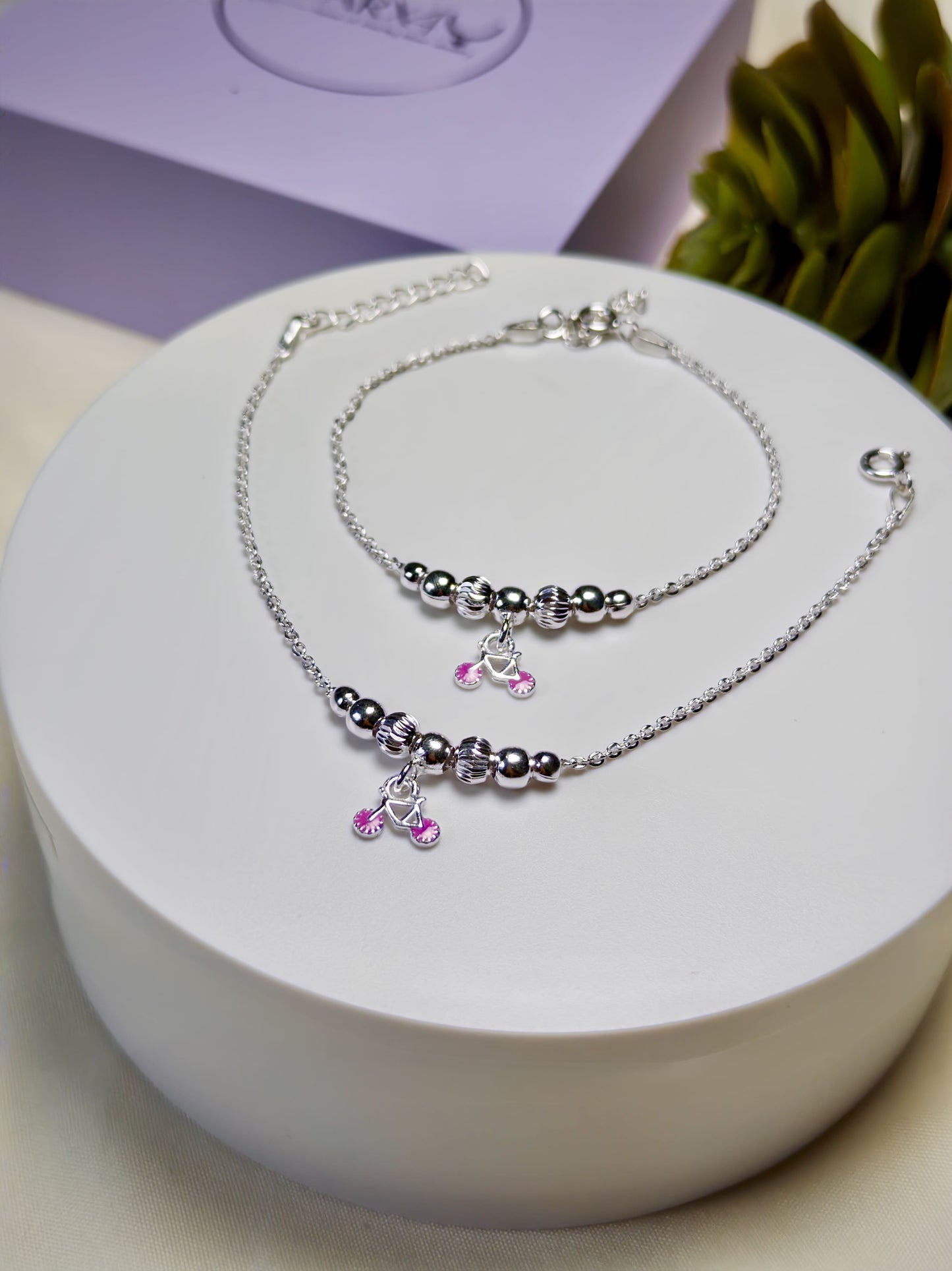 Kids silver anklets with purple charms on a white surface
