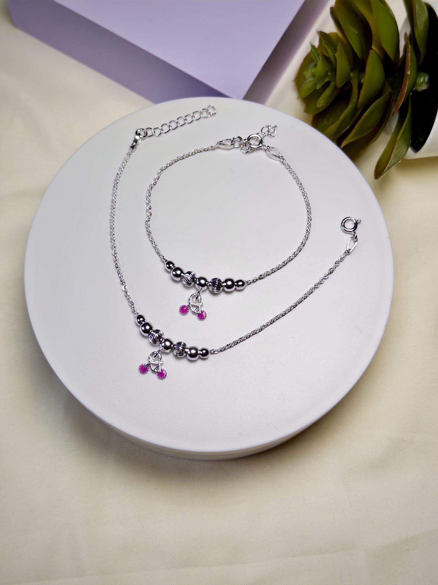 Set of kids silver anklets with purple charm on a white plate
