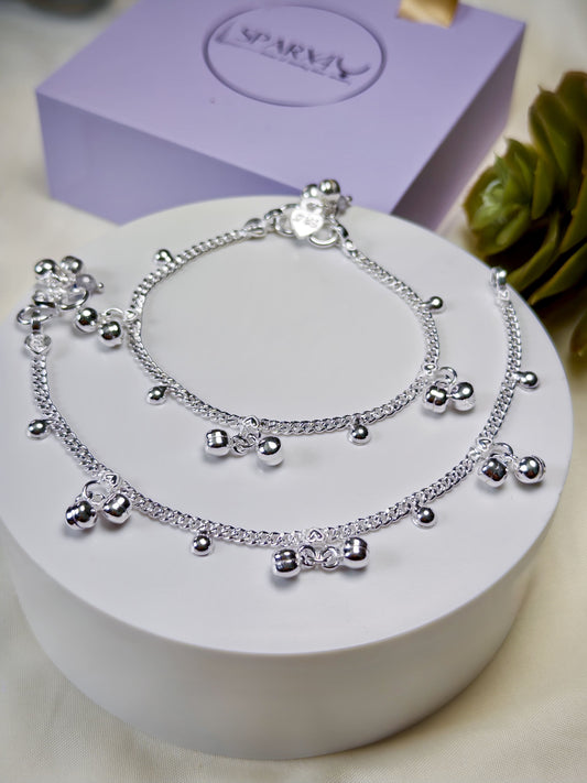 Kids silver anklets with heart-shaped charms on a white surface with a purple box in the background