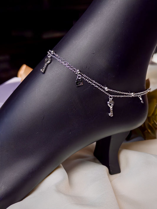 Silver anklet with charms on a black mannequin foot against a neutral background