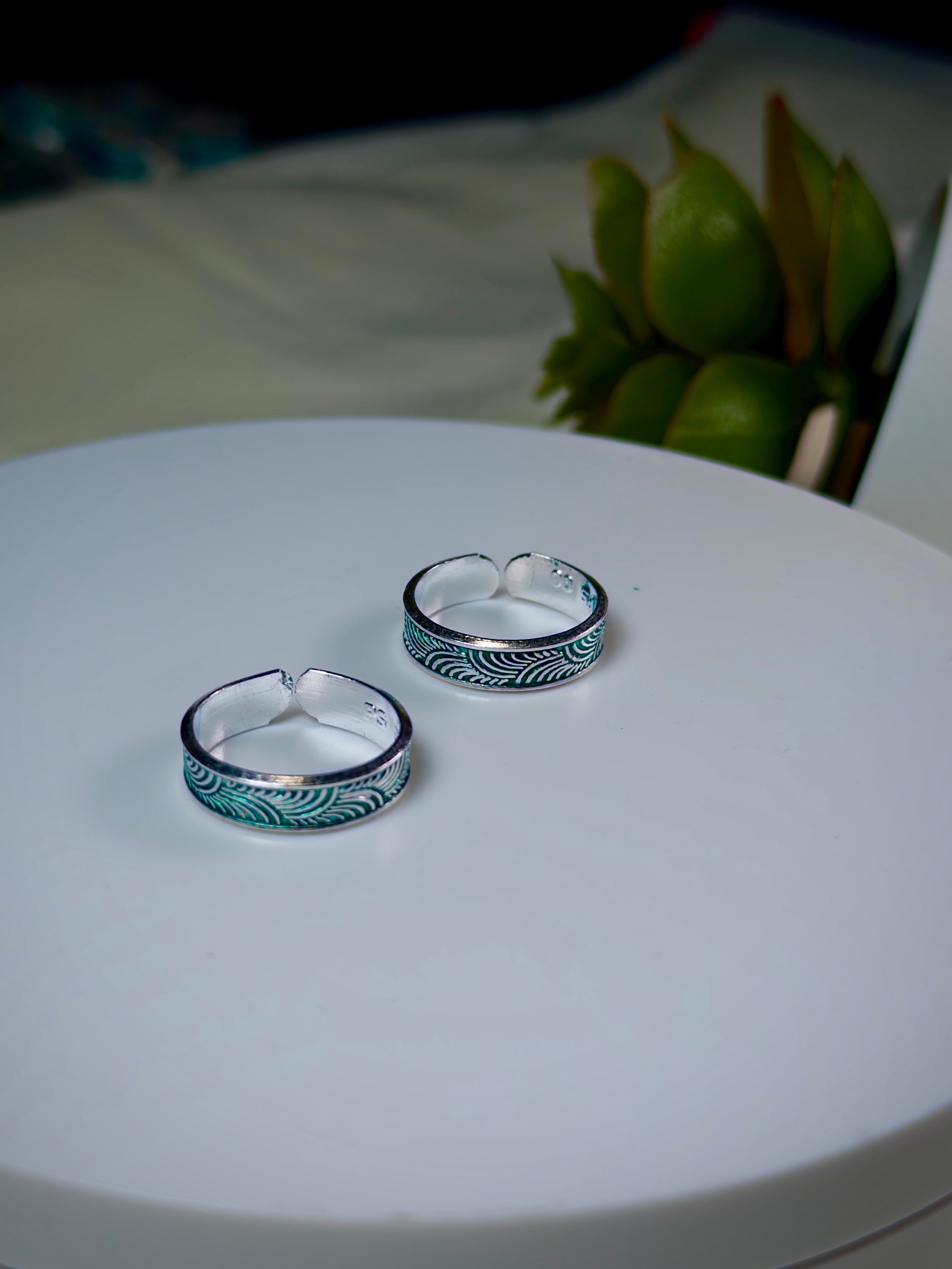 Two silver toe rings with green patterns on a white surface.