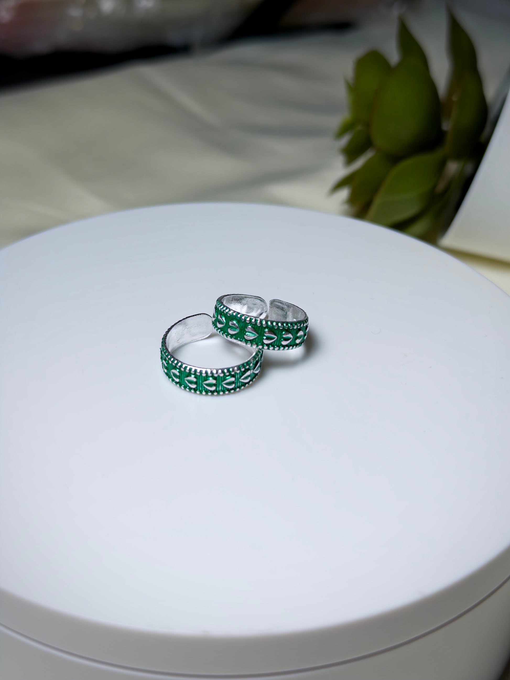Two silver toe rings with green enamel on a white surface.