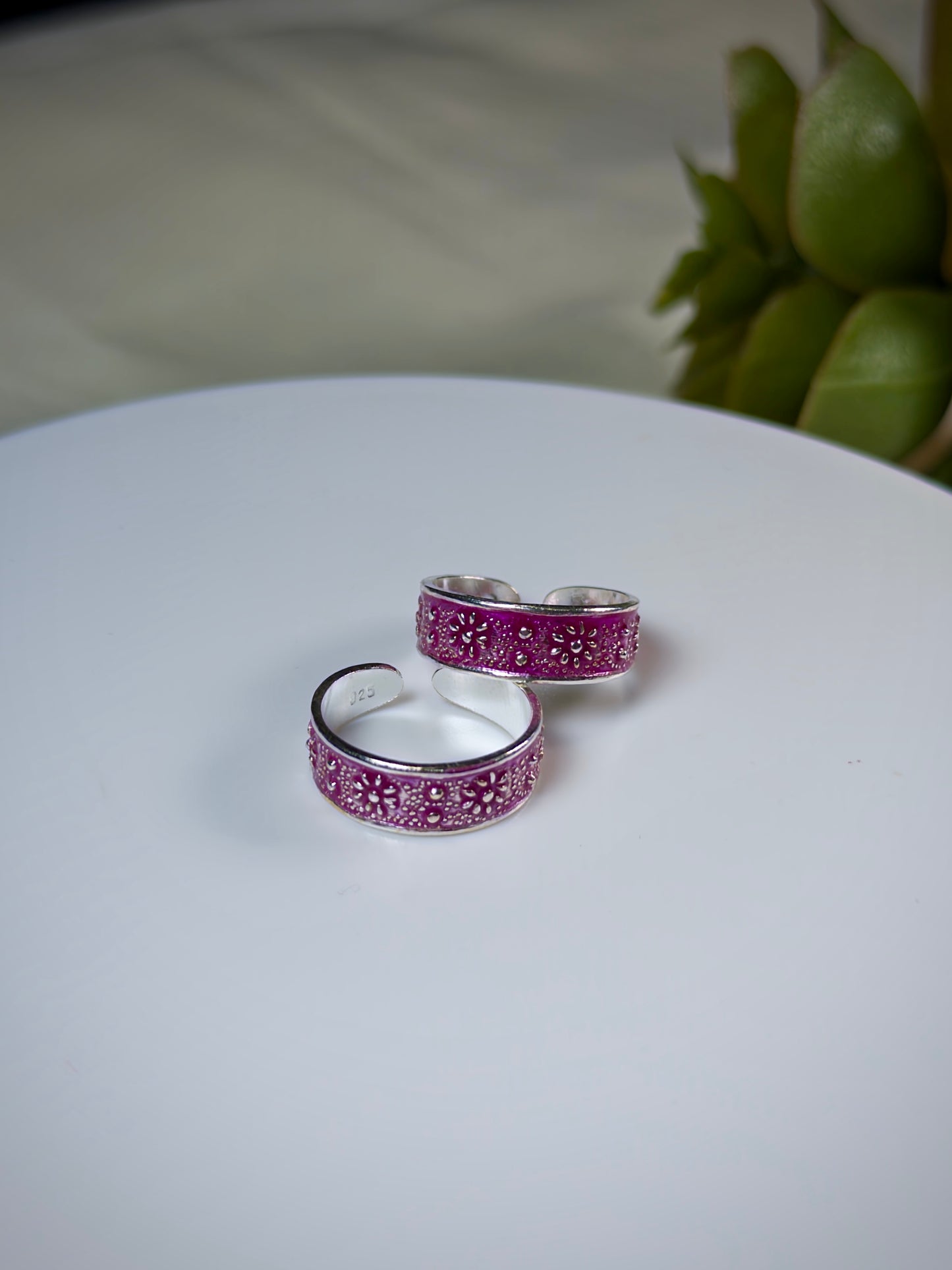 Two silver toe rings with purple accent on a white surface.