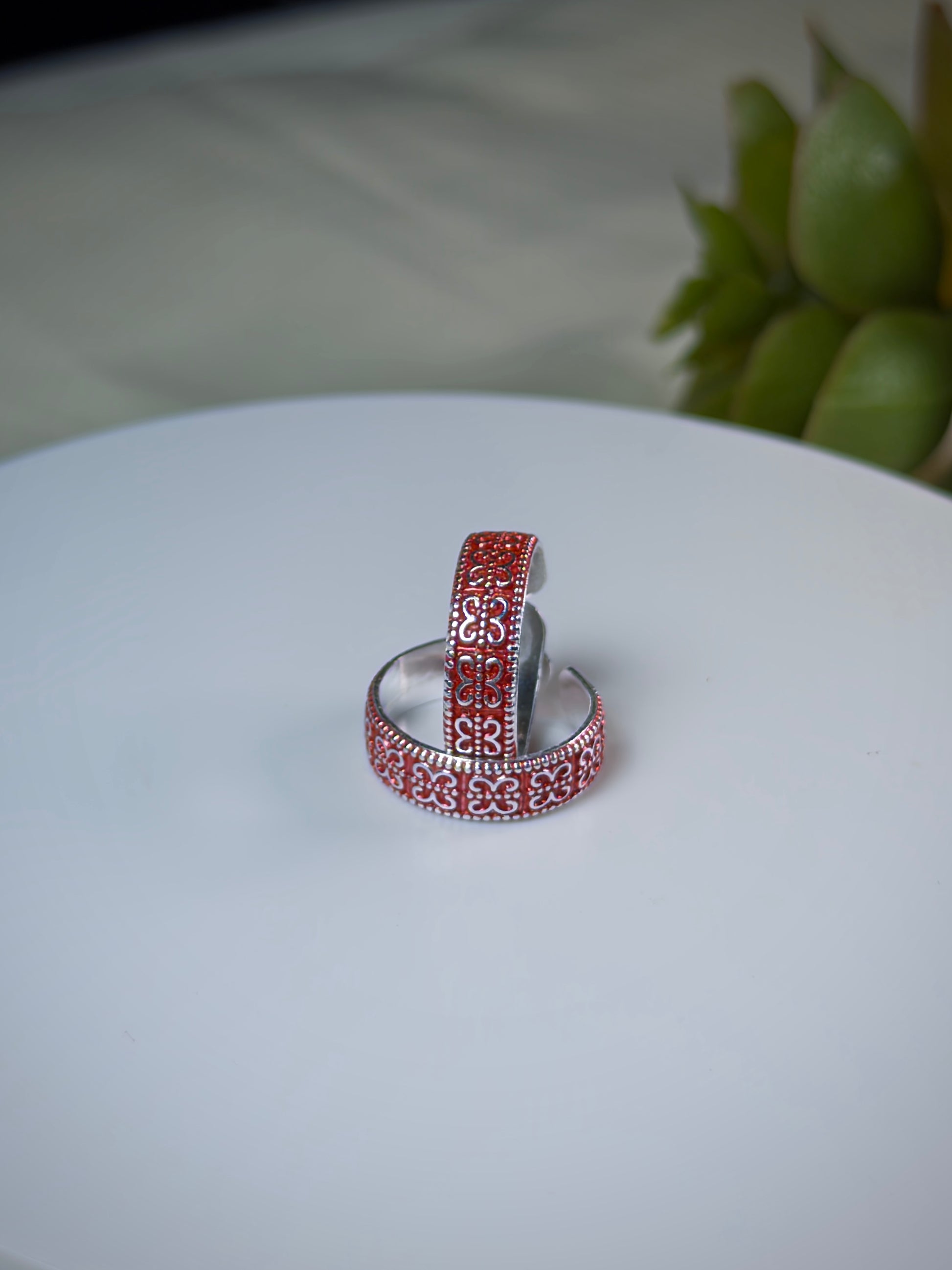 Two silver toe rings with red pattern on a white surface.