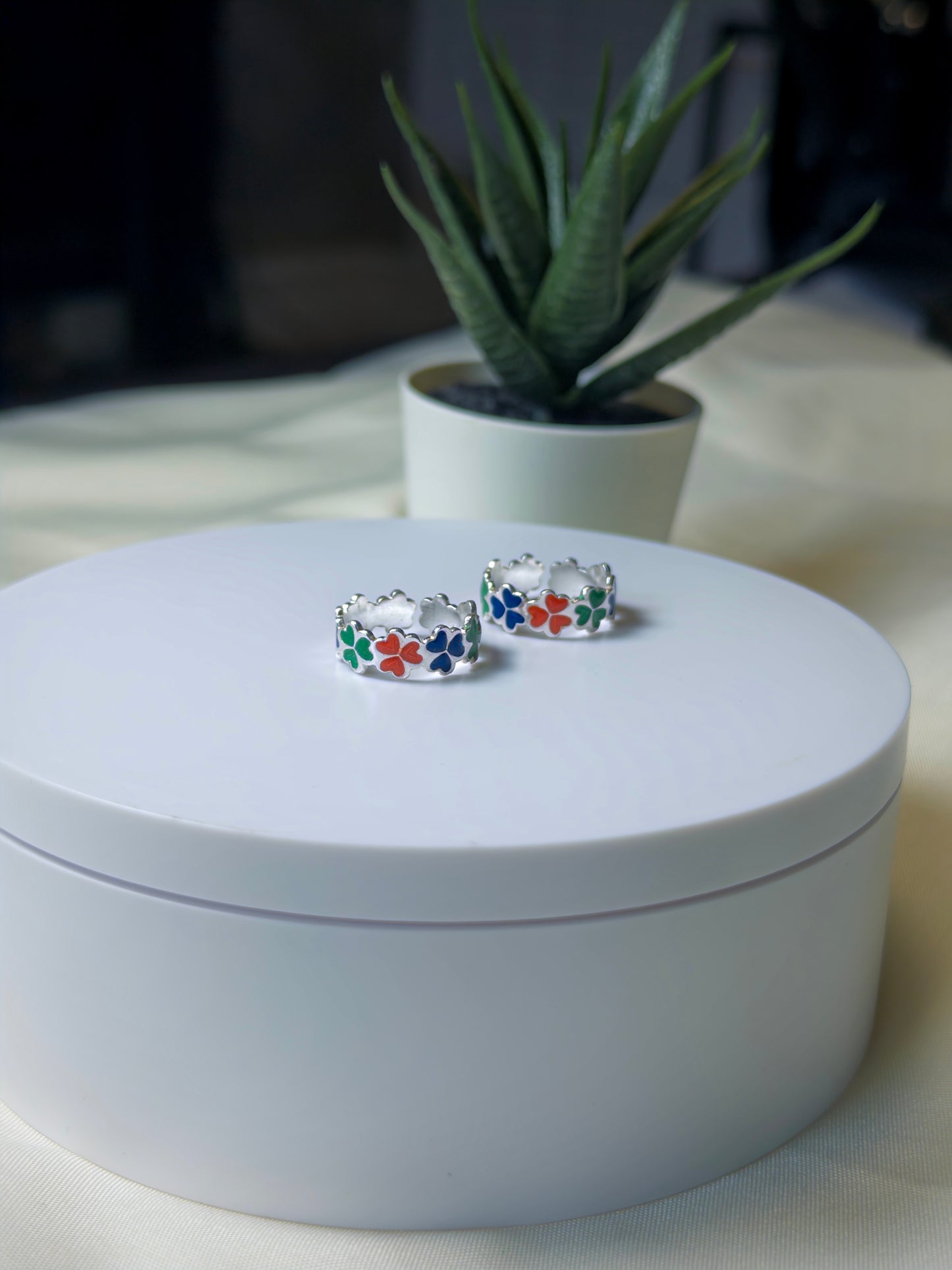 Silver toe rings with colorful stones on a white surface, with a plant in the background.