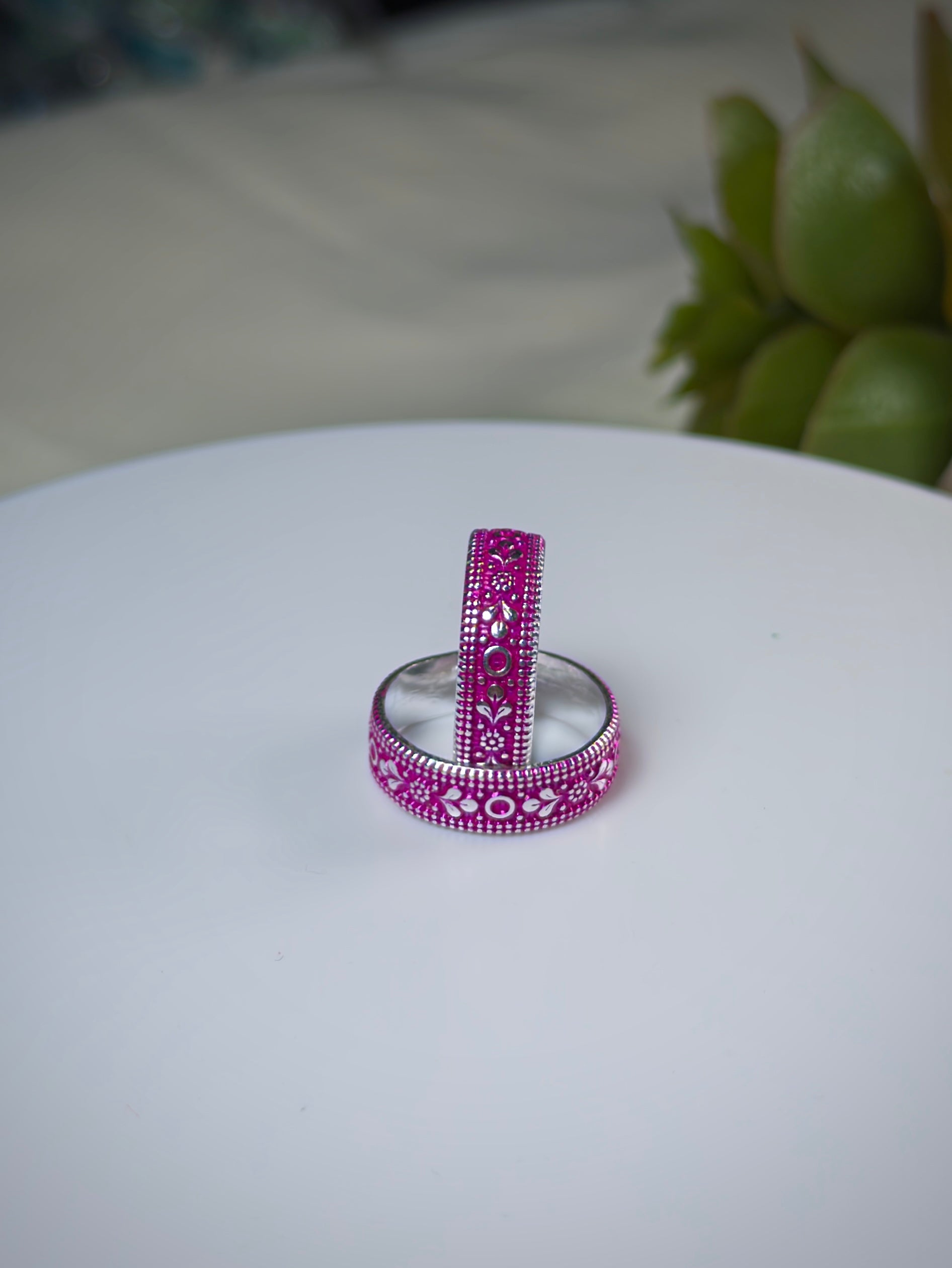 Two pink and silver toe rings on a white surface with a blurred green plant in the background.