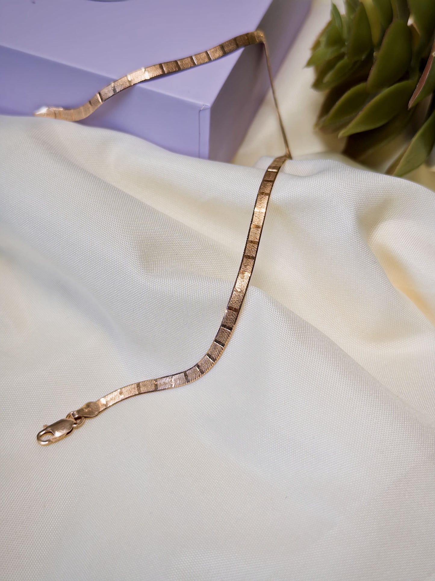 Rose gold anklet on a light fabric surface with a blurred background