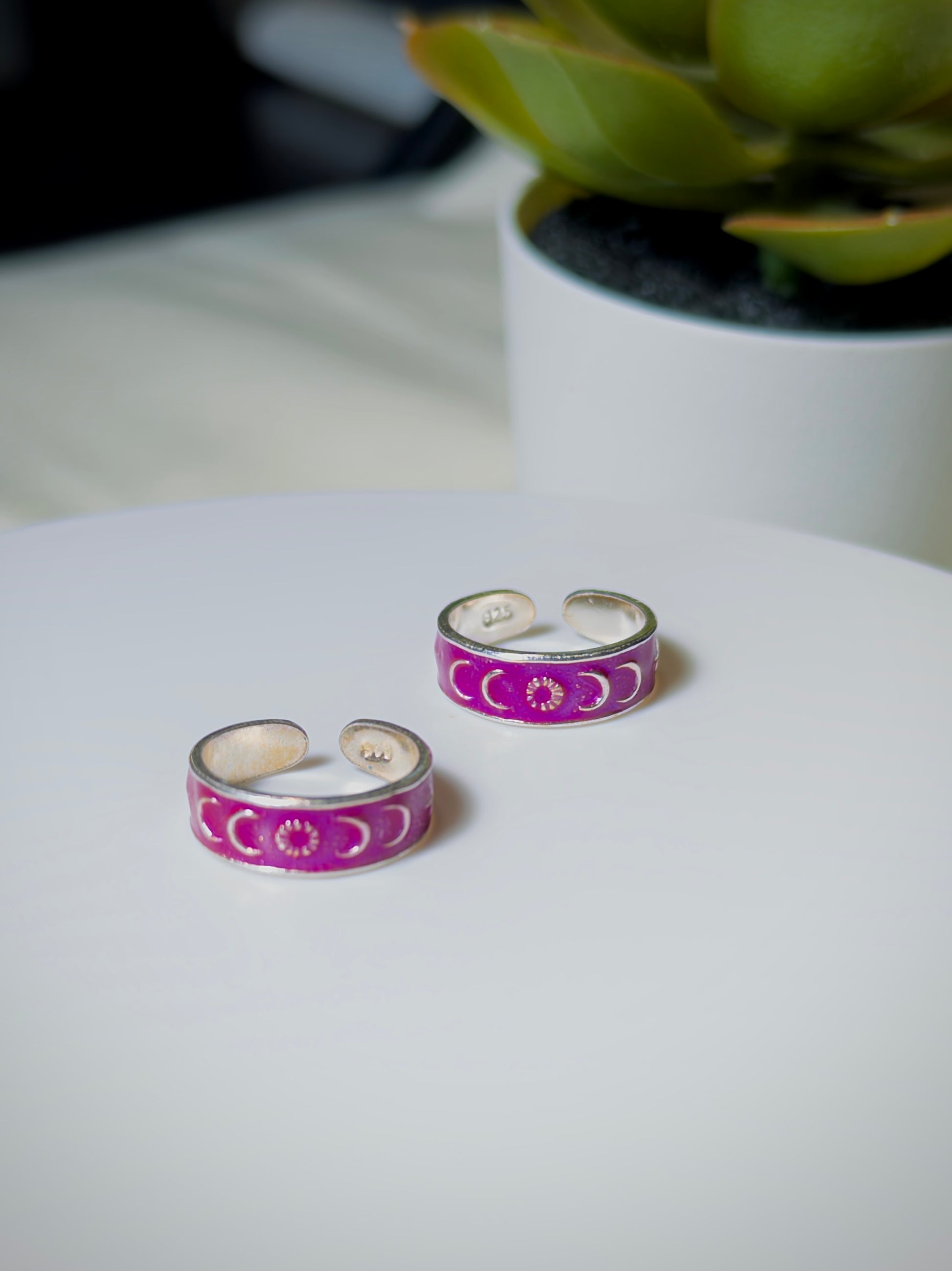 Pair of pink and silver toe rings on a white surface with a plant in the background