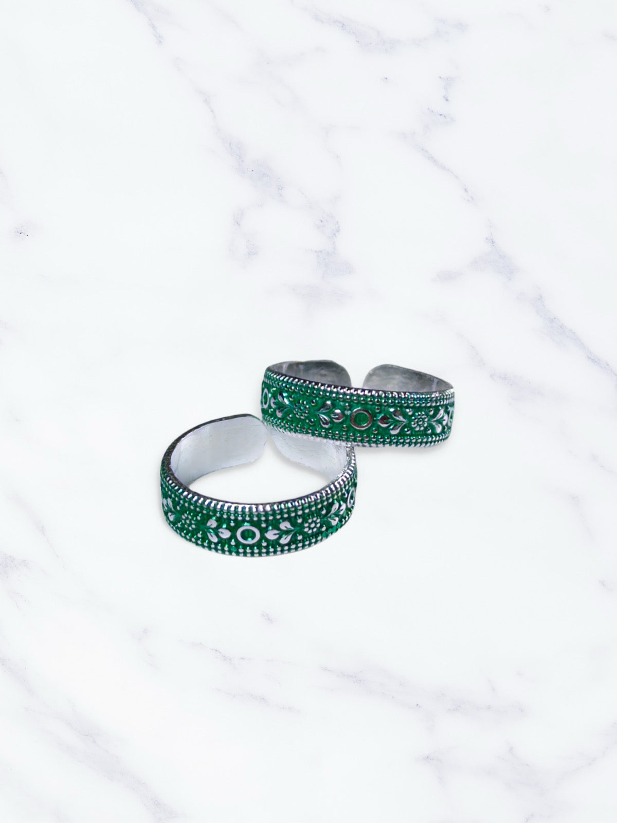 Two green and silver toe rings on a white marble surface