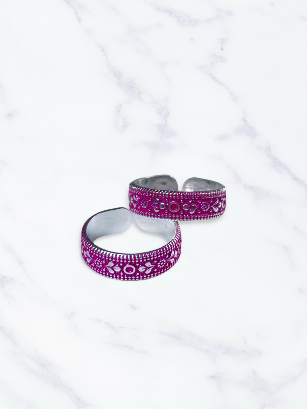 Two silver and pink toe rings on a white marble surface