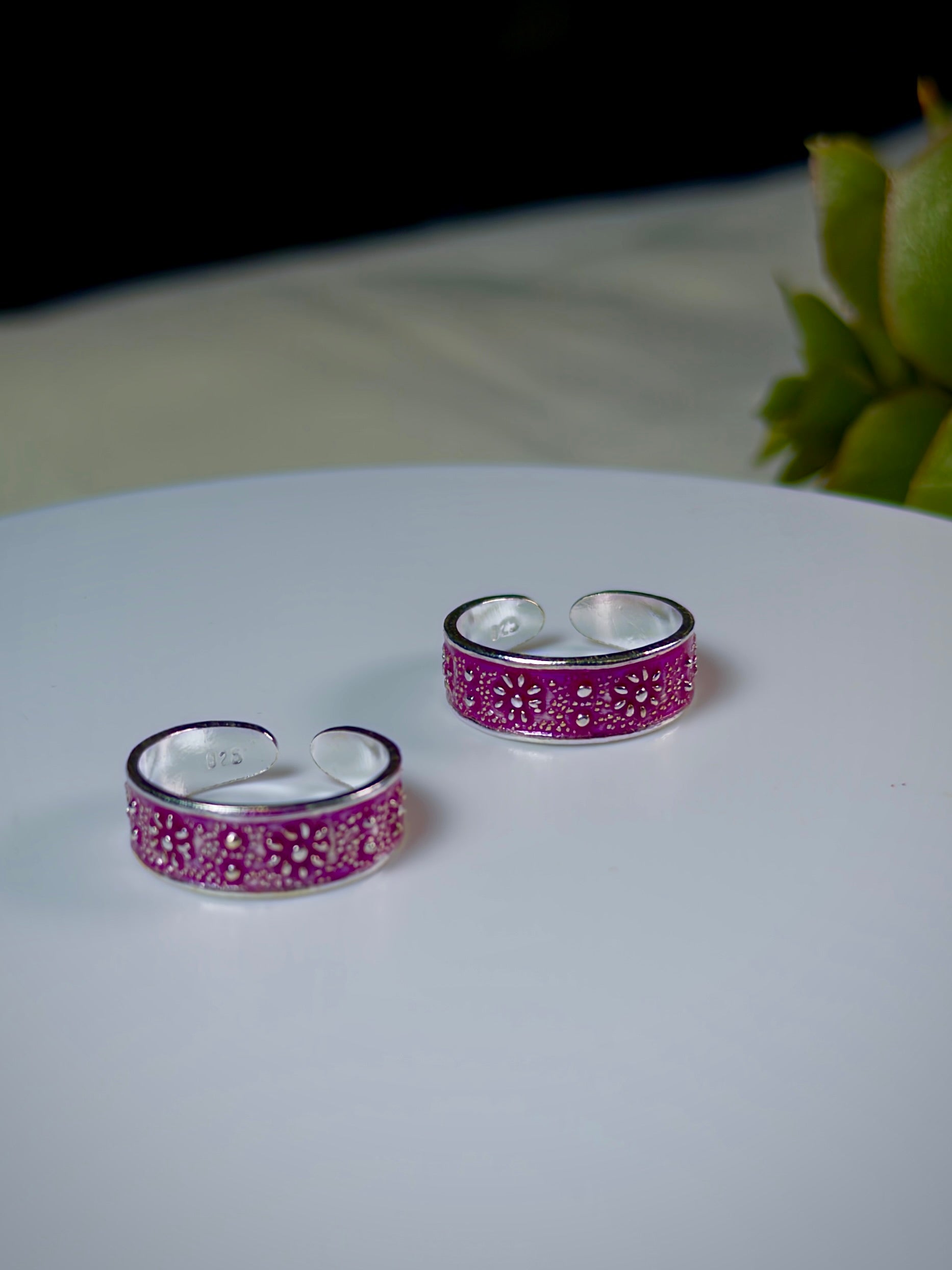 Pair of silver toe rings with pink floral patterns on a white surface.