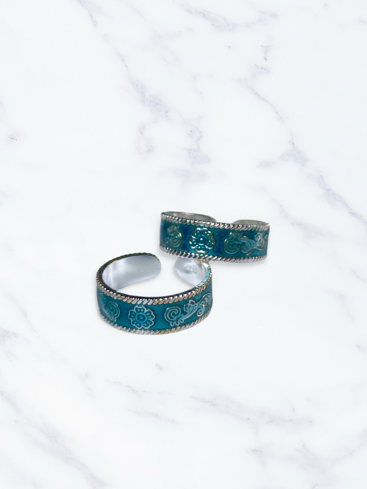 Two turquoise patterned toe rings on a white marble surface