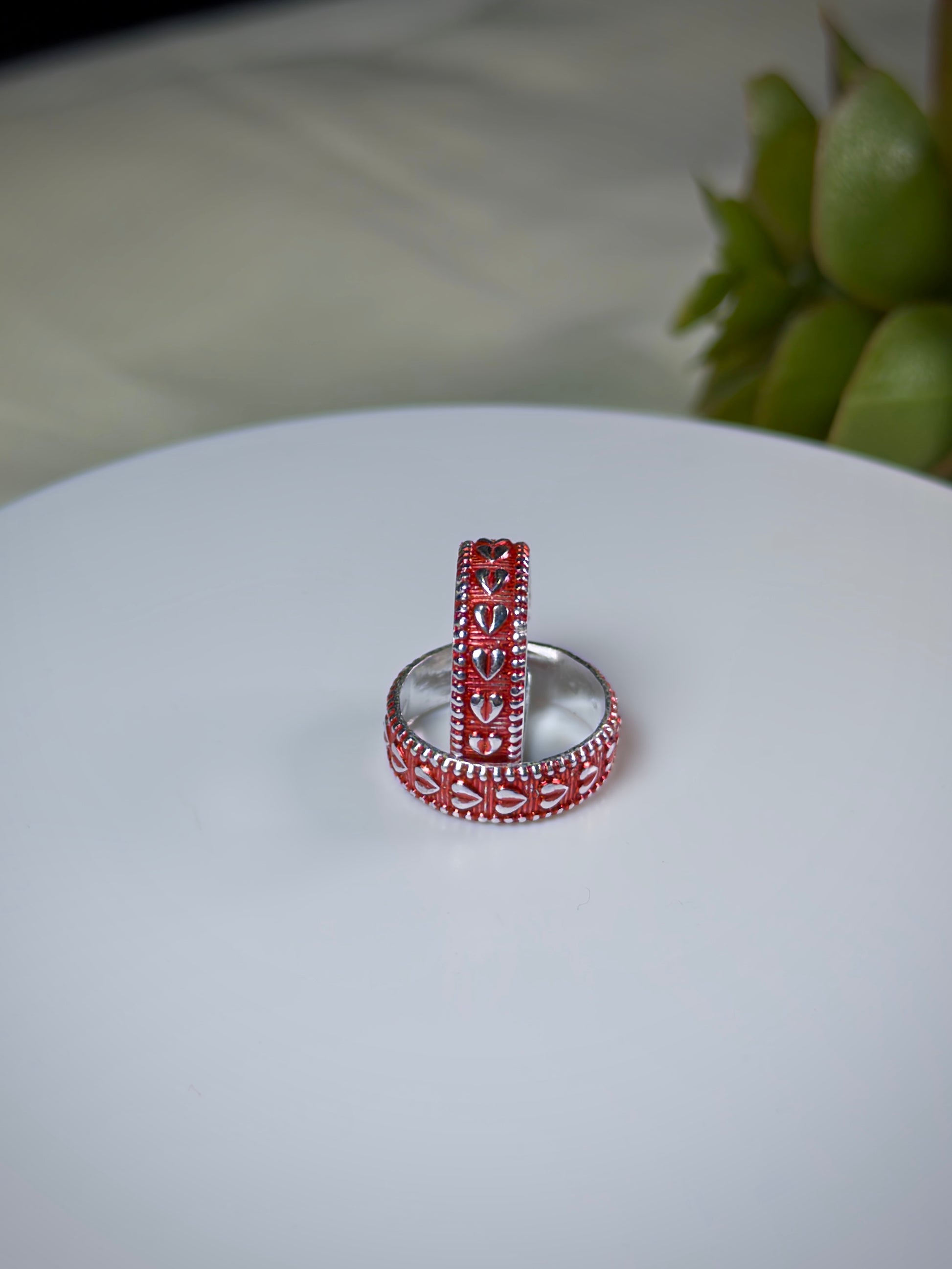 Silver ring with red heart toe rings on a white surface