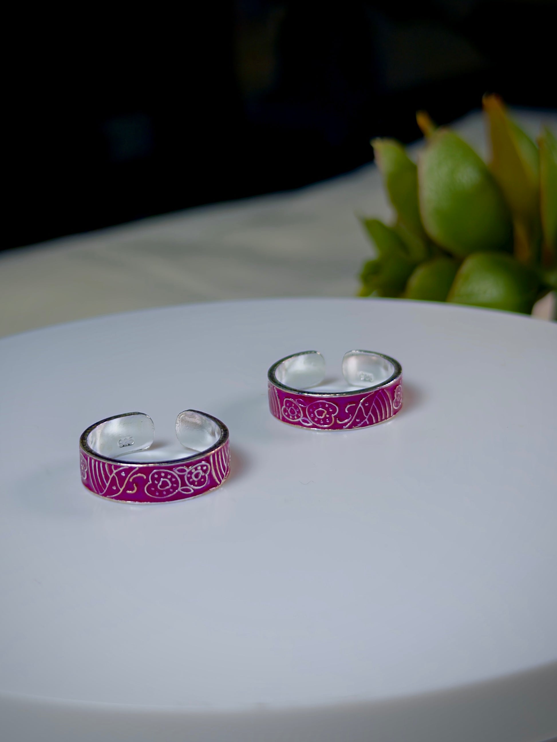 Silver toe rings with purple patterns on a white surface.