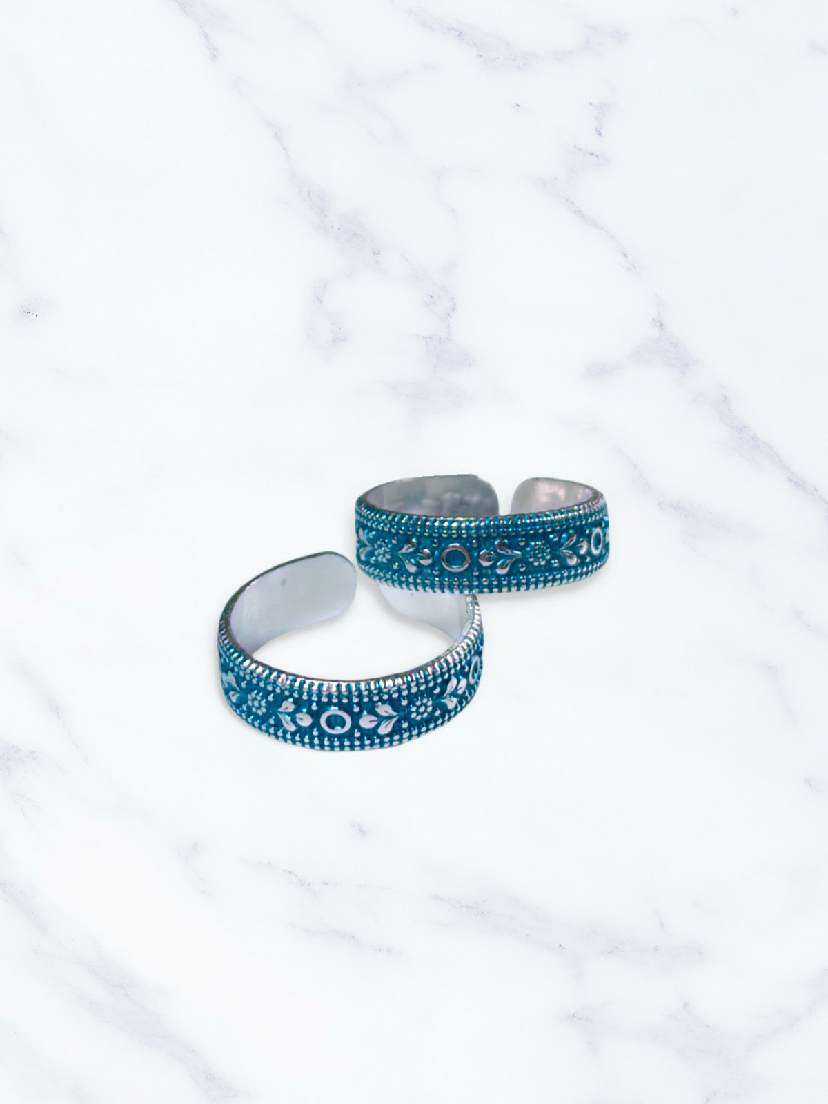 Two blue and silver patterned toe rings on a white marble surface