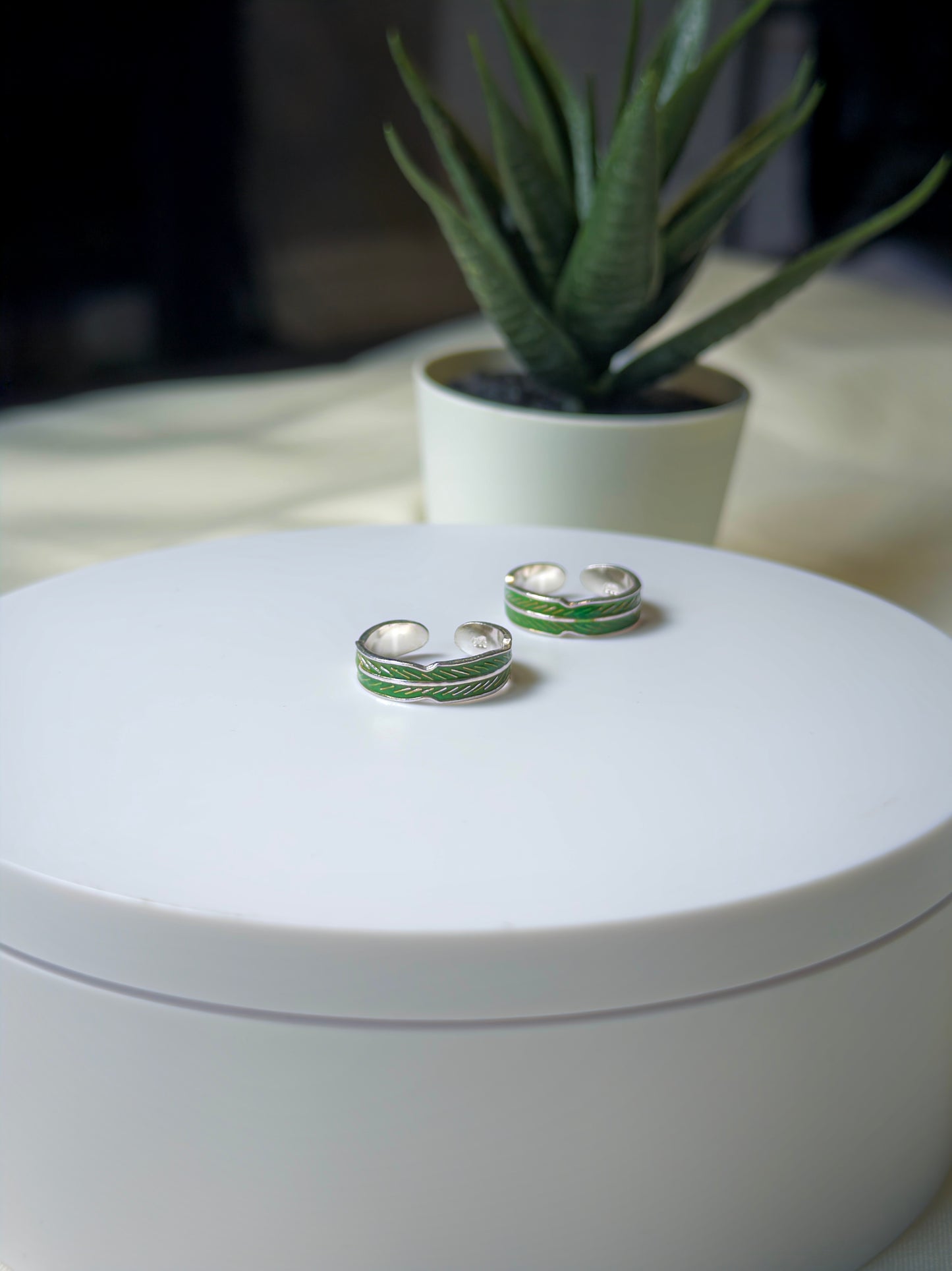 Silver and green toe rings on a white surface with a plant in the background