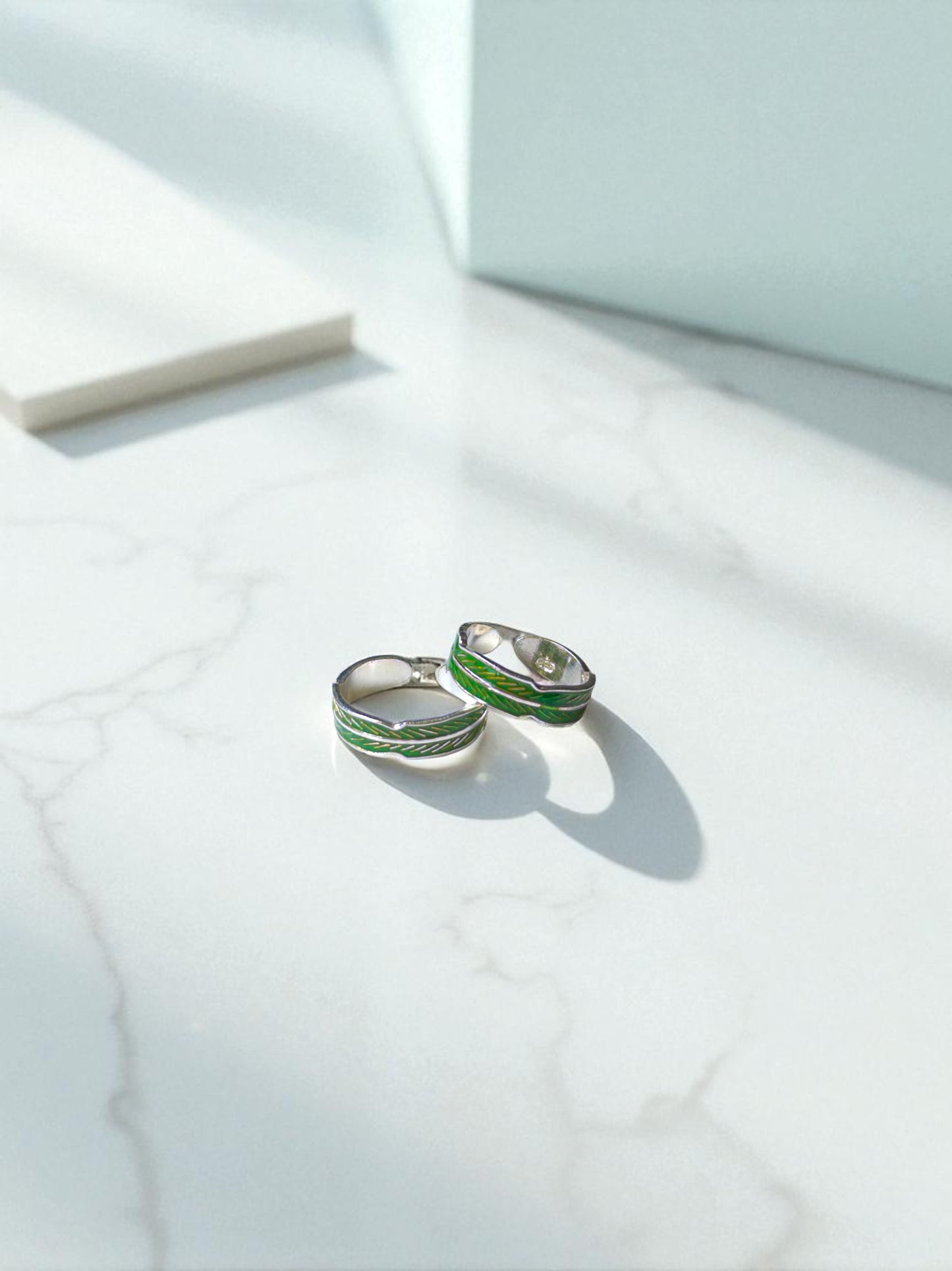 Silver toe rings with green accents on a light marble surface