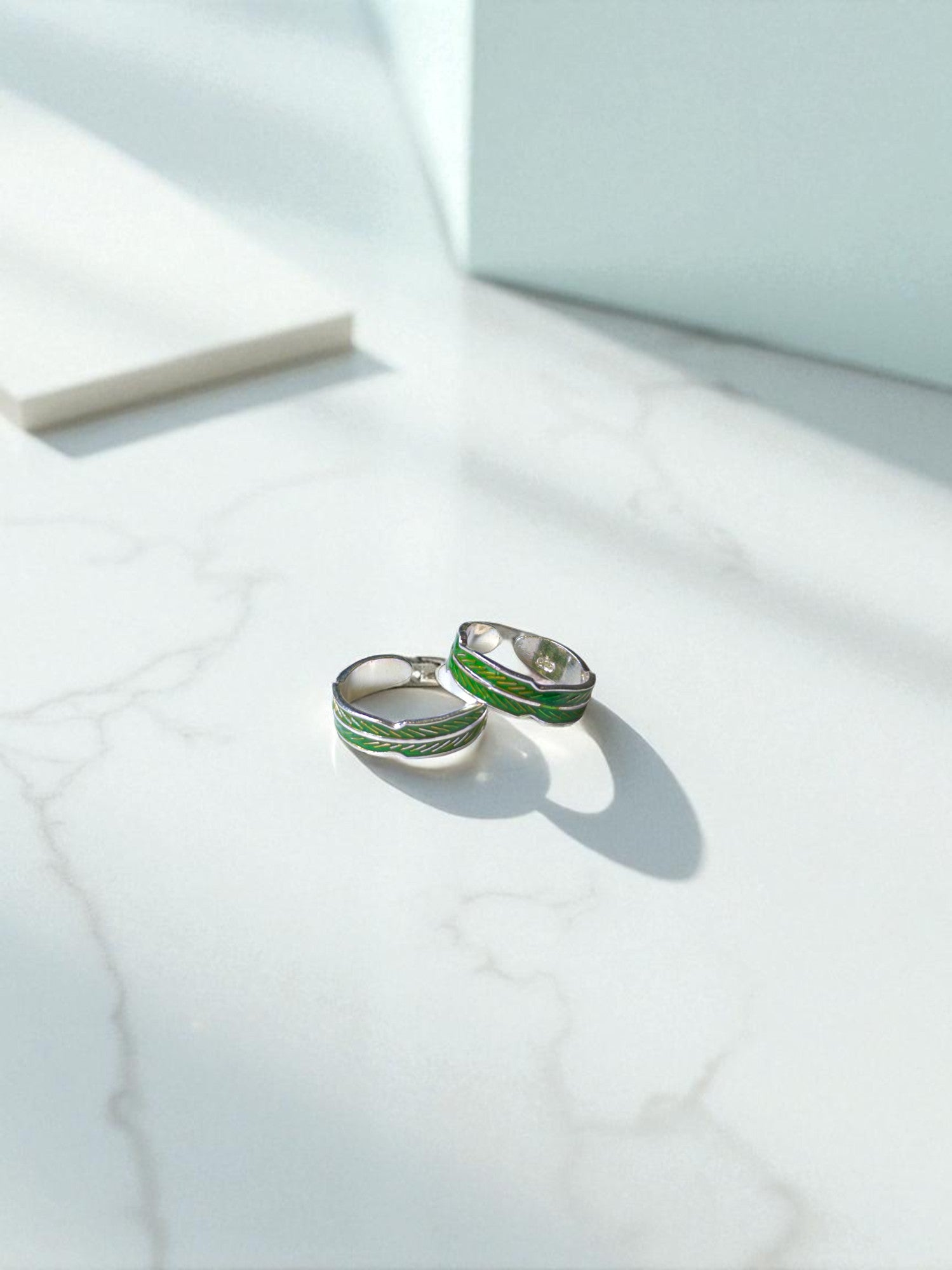Silver toe rings with green accents on a light marble surface