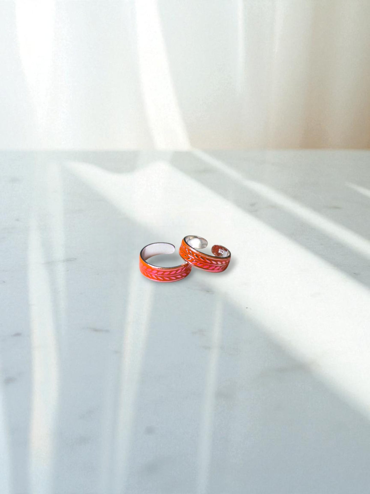 Two orange toe rings on a marble surface with a white curtain in the background