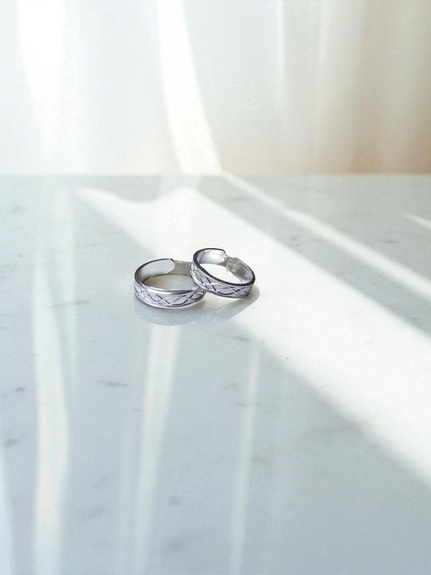 Two silver toe rings on a marble surface with soft lighting
