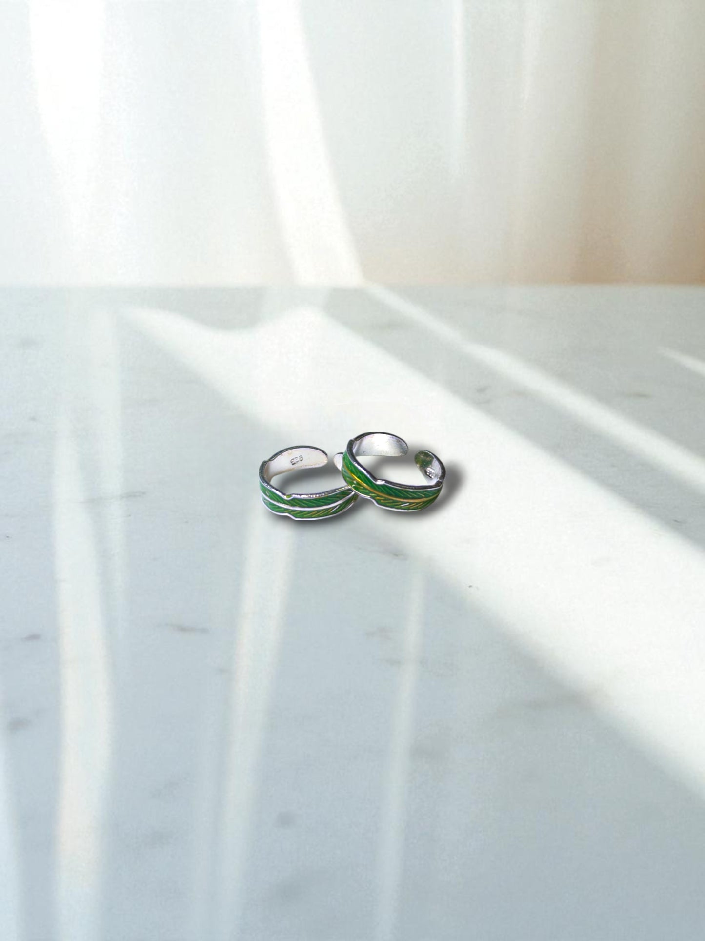 Small toe rings with green accents on a marble surface
