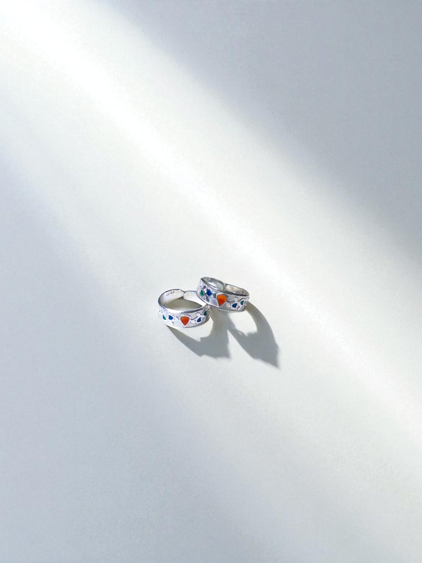 Two silver rings with colorful heart designs on a white background