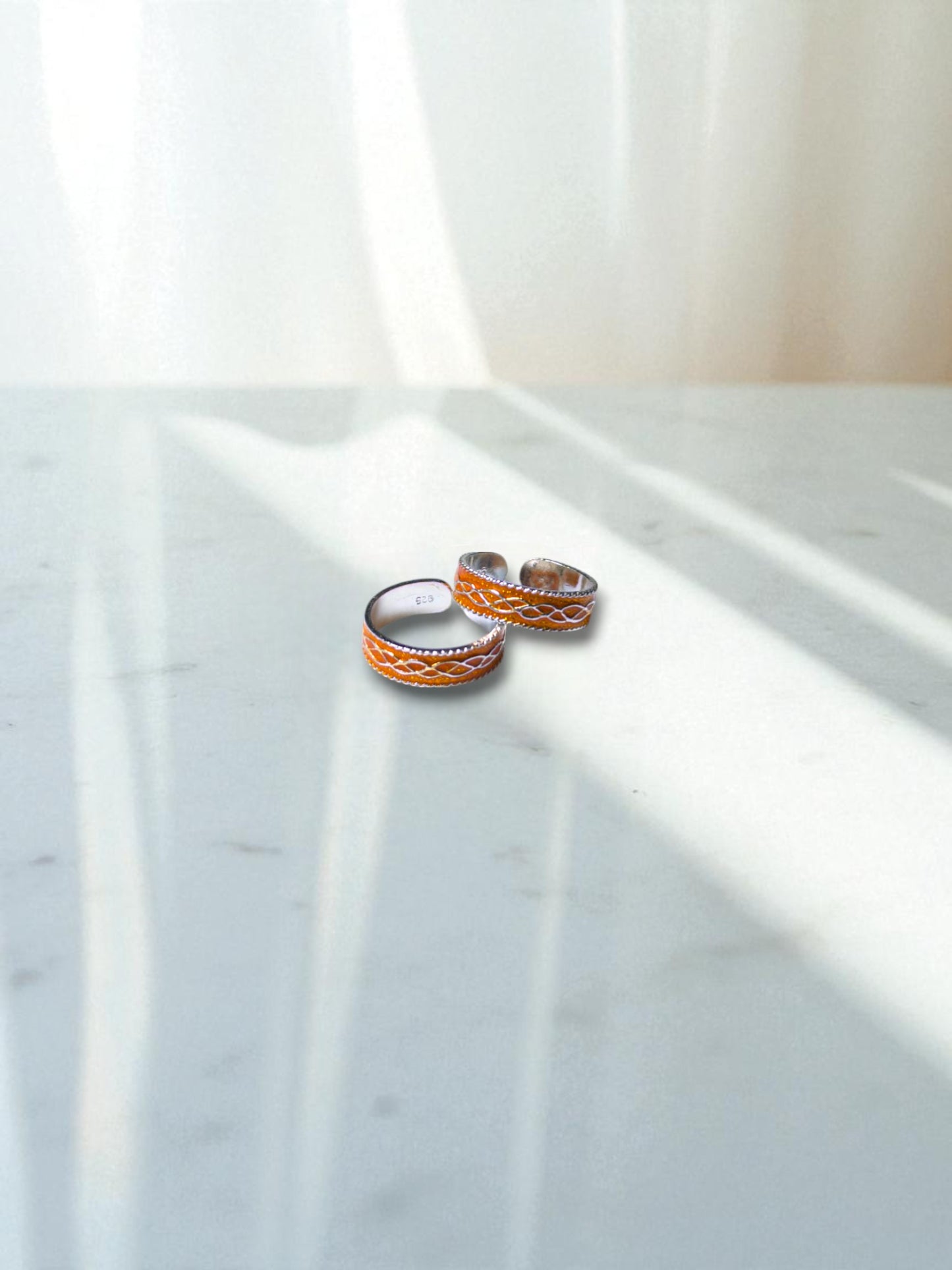 Two silver toe rings on a marble surface with soft lighting