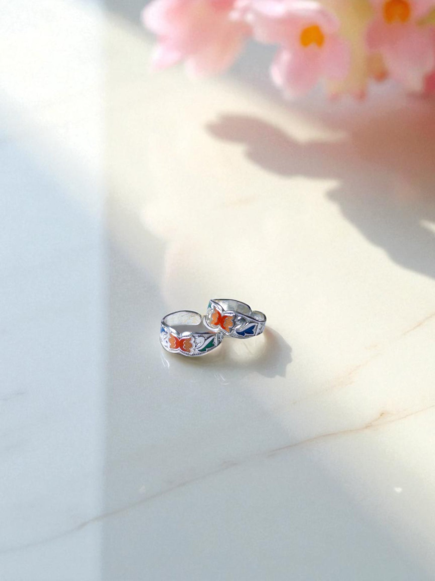 Silver toe rings with floral designs on a light surface