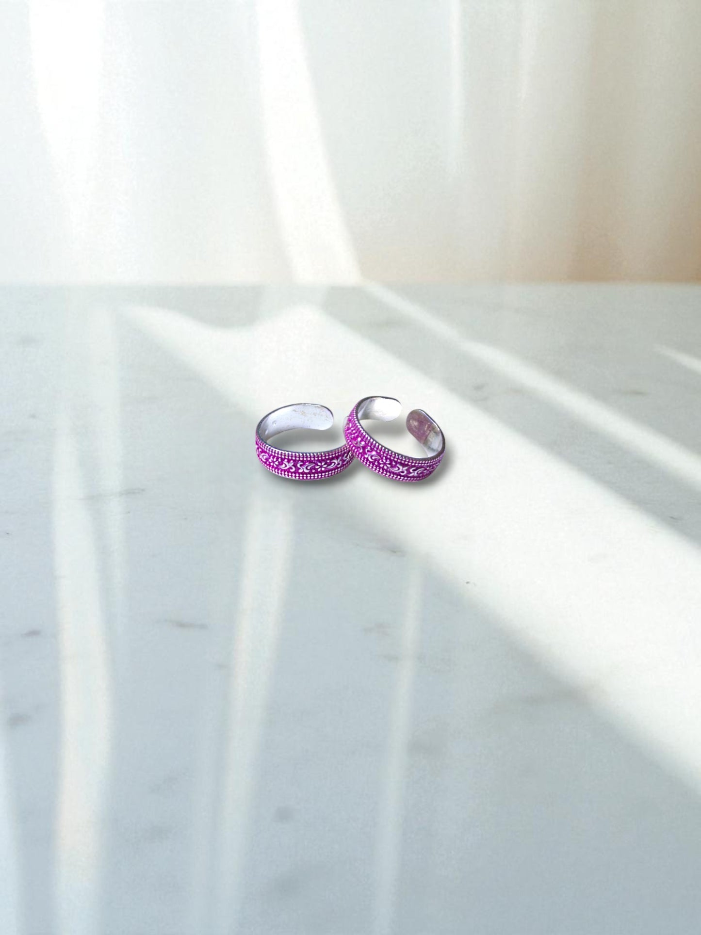 Two pink toe rings with intricate designs on a marble surface