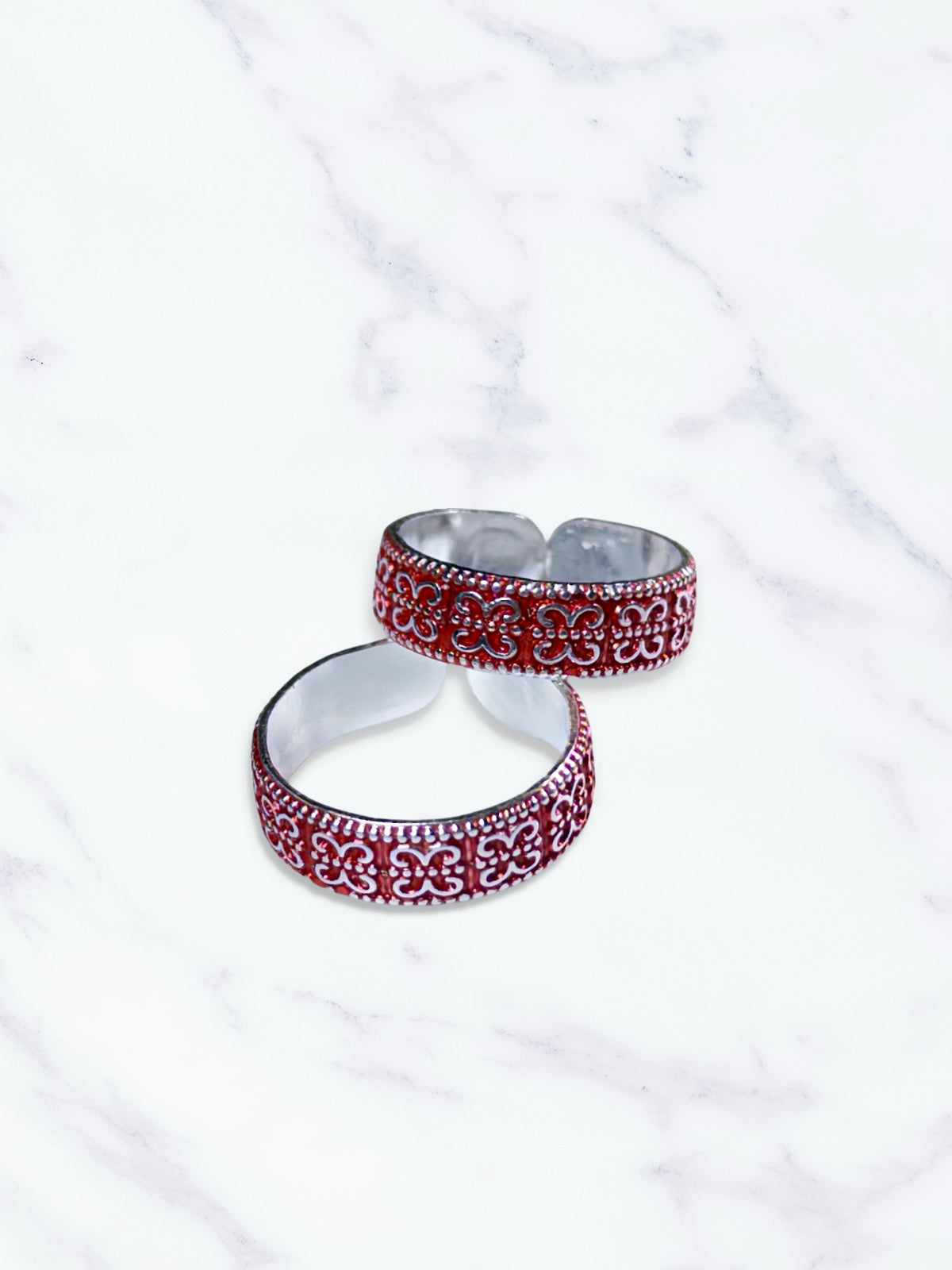 Two silver and red patterned toe rings on a white marble surface