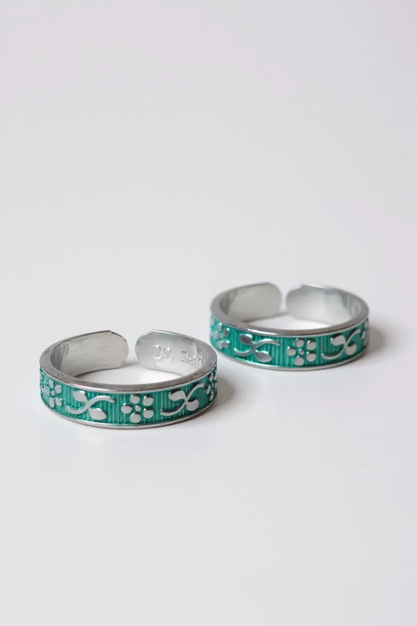Two silver toe rings with green enameled patterns on a light gray background