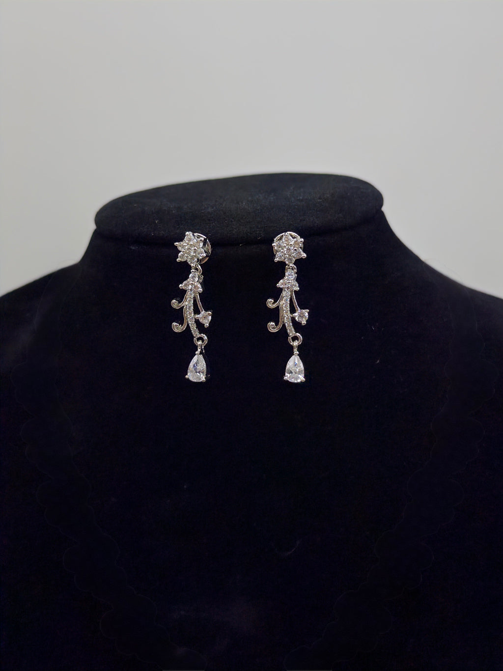 Pair of silver earrings on a black velvet stand with a plain background