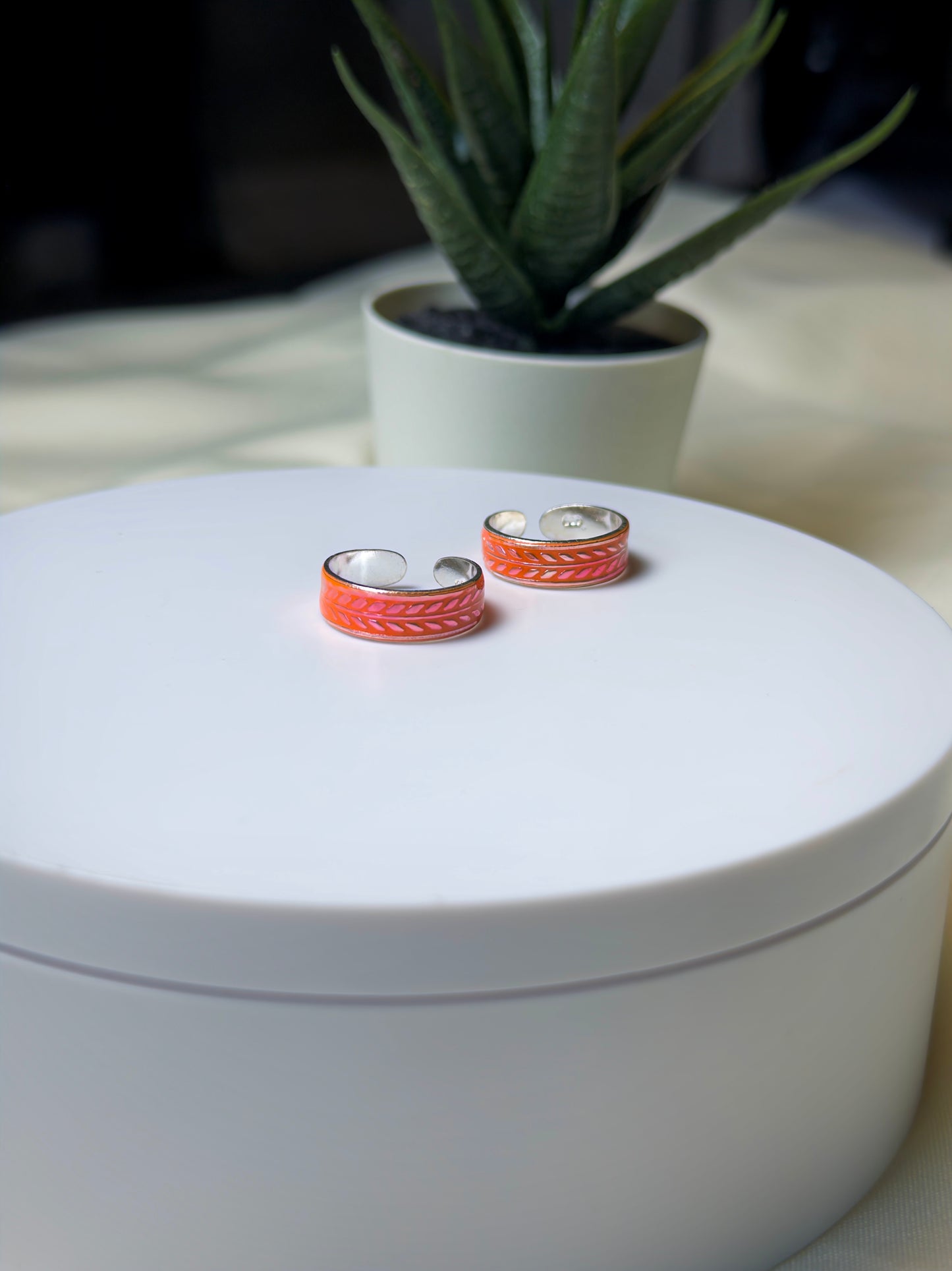 Pair of toe rings on a white surface with a plant in the background
