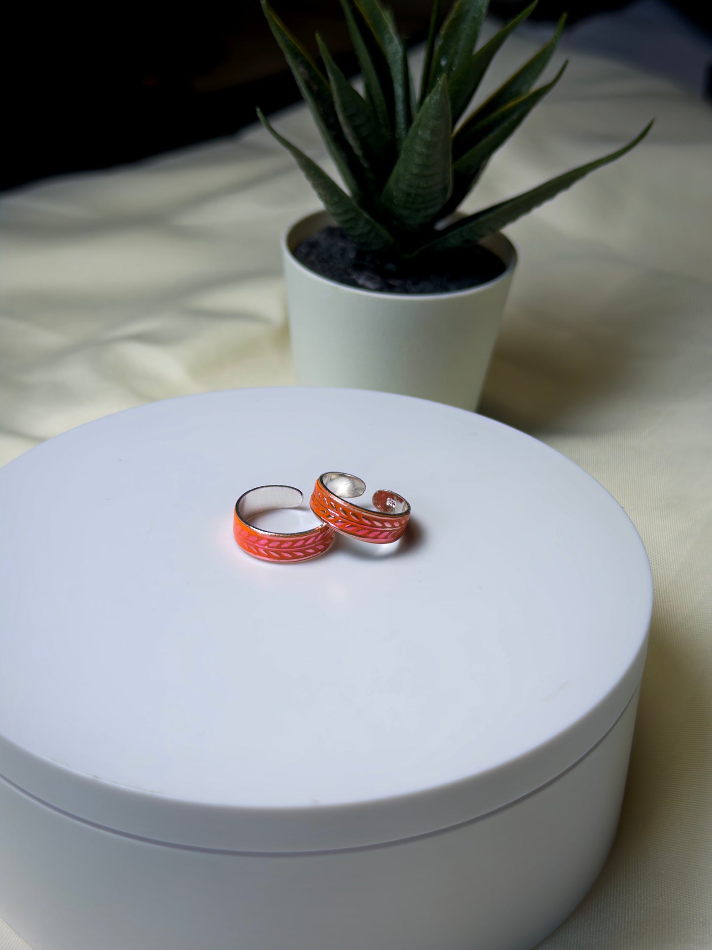 Two orange toe rings on a white surface with a plant in the background