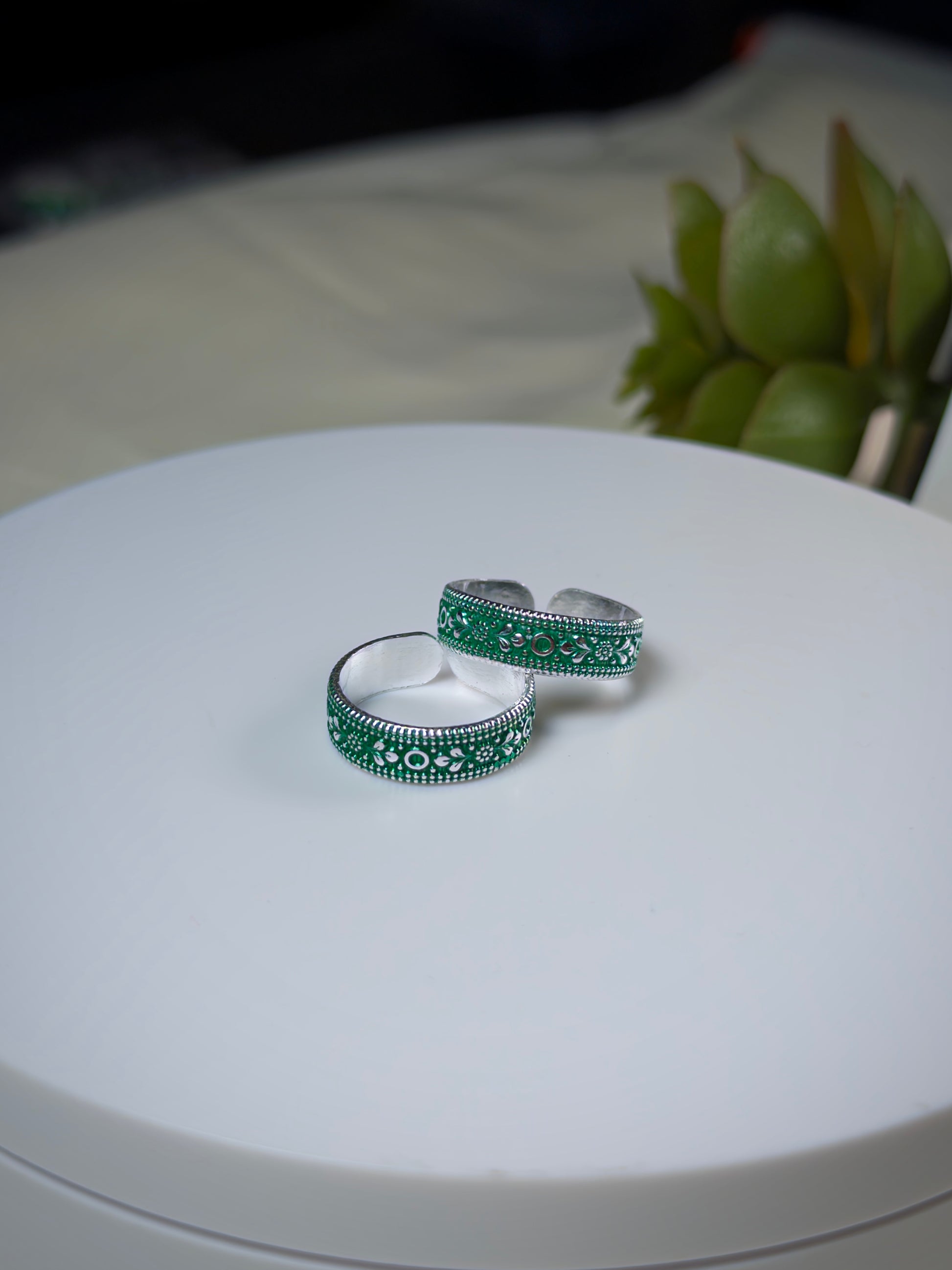 Two silver toe rings with green gemstones on a white surface.