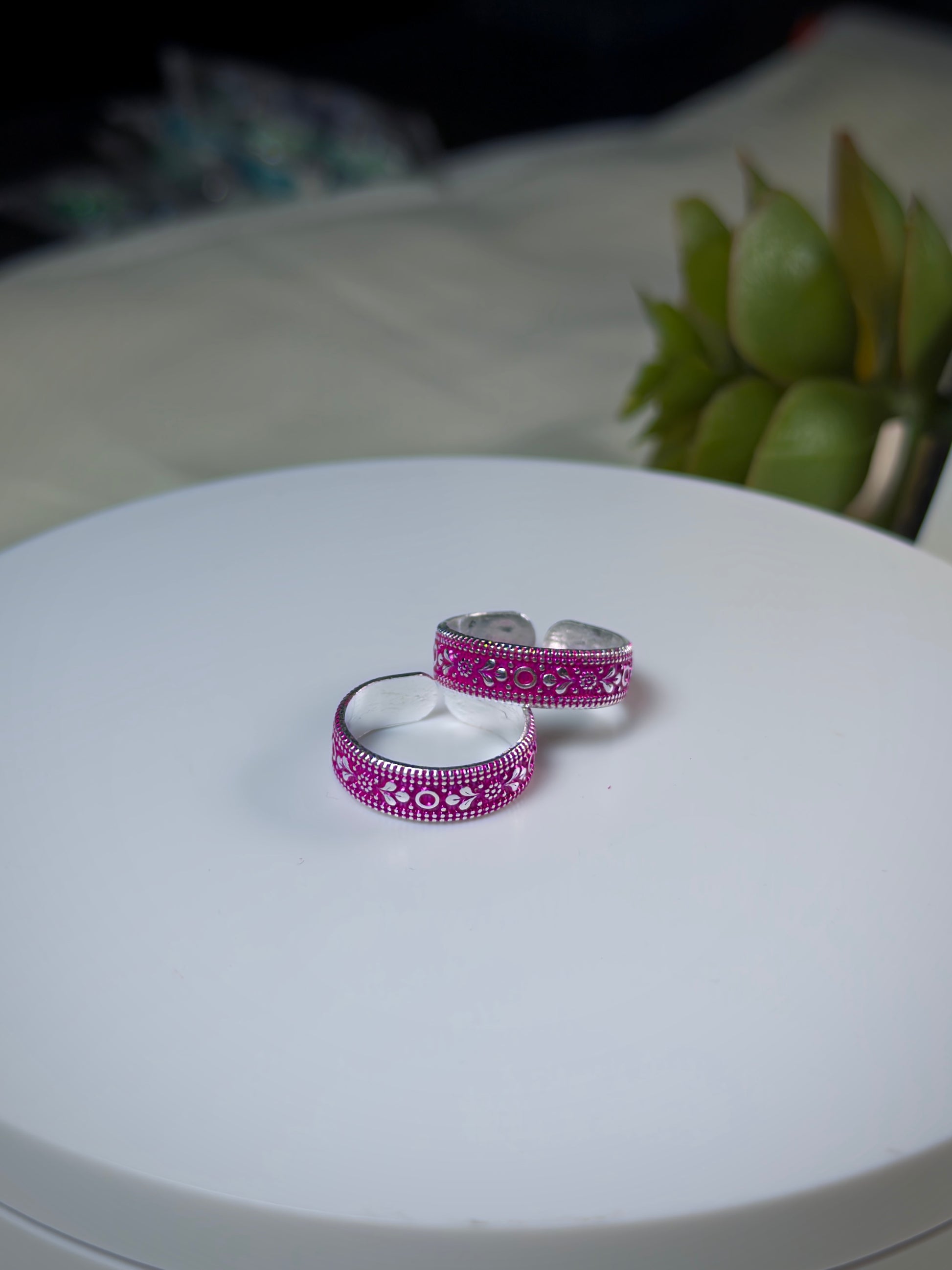 Two silver toe rings with pink gemstone settings on a white surface.
