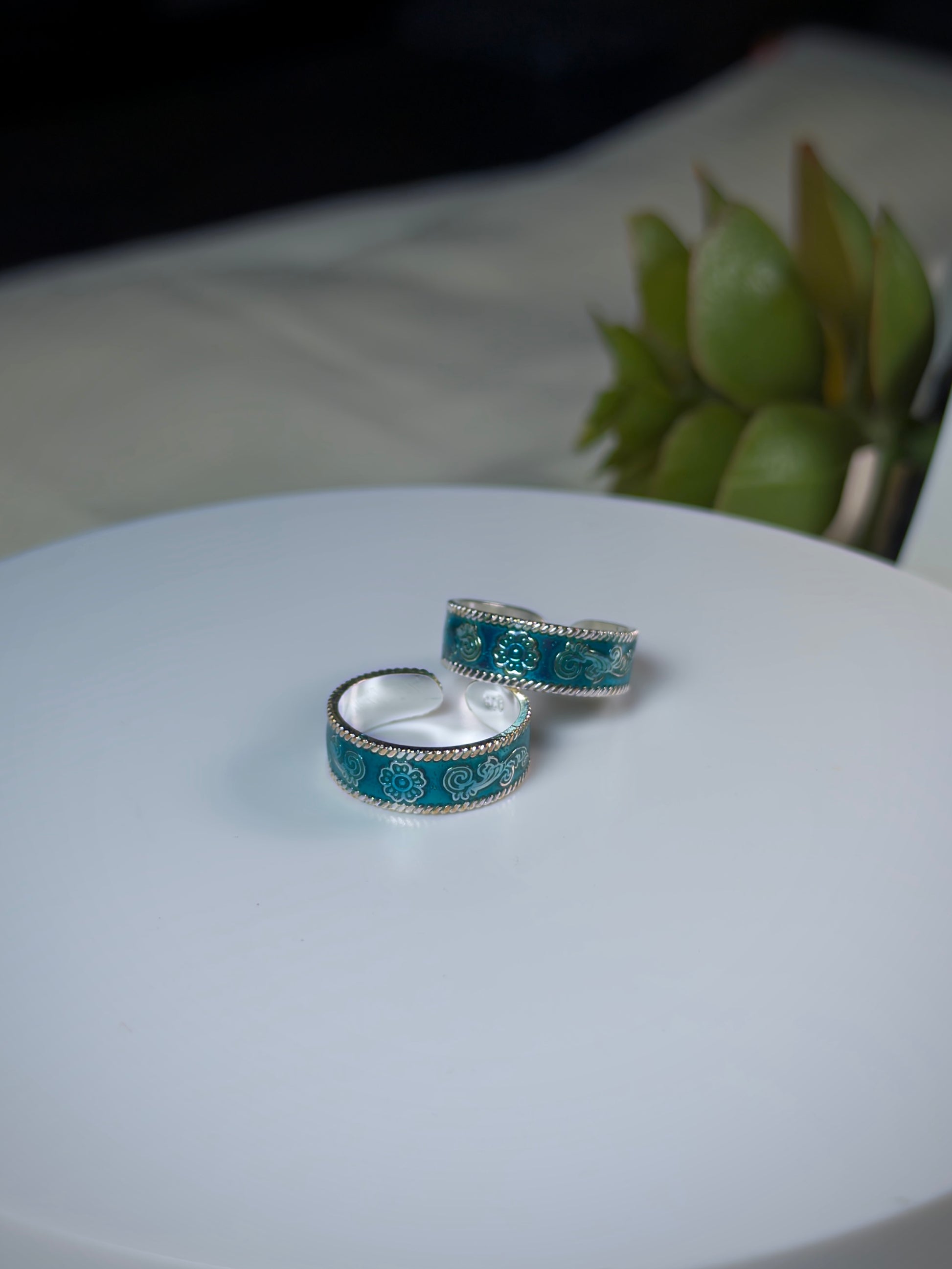 Two turquoise toe rings with silver patterns on a white surface.