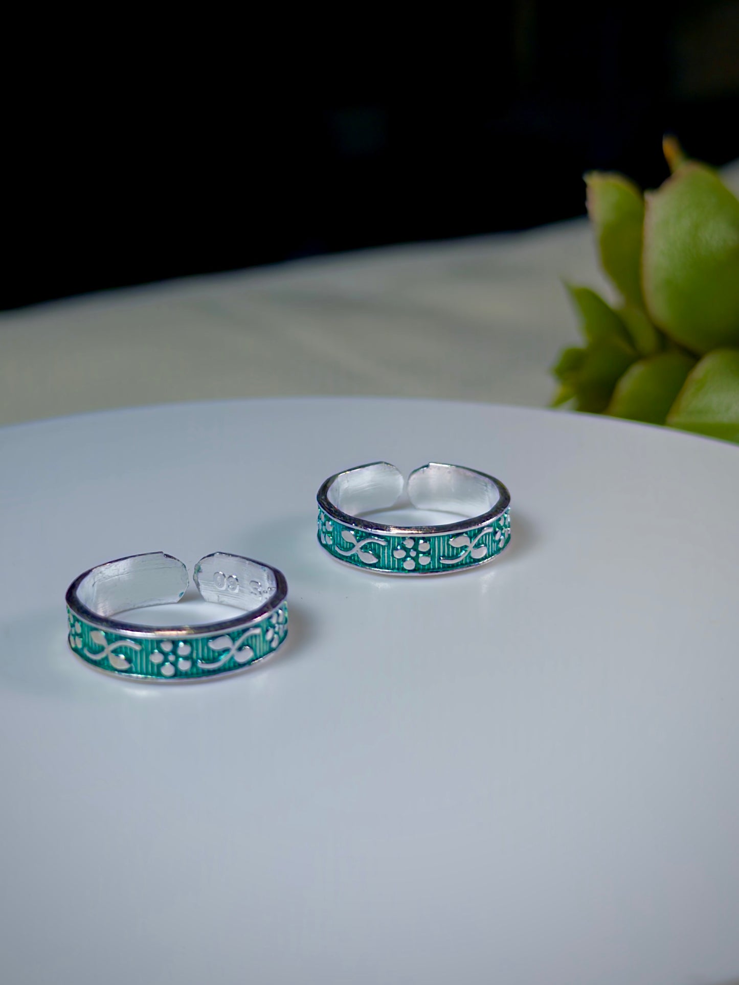 Two silver toe rings with green floral patterns on a white surface.