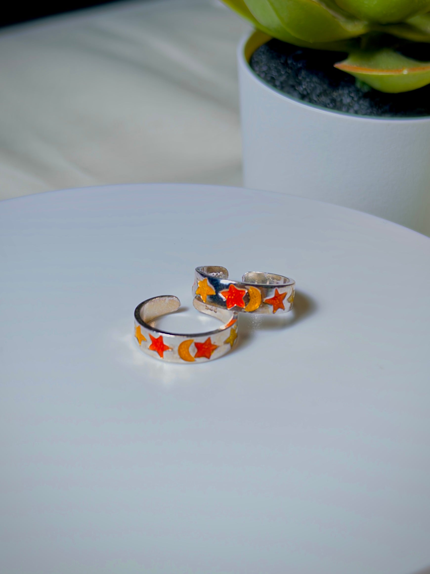 Two silver toe rings with colorful star patterns on a white surface.